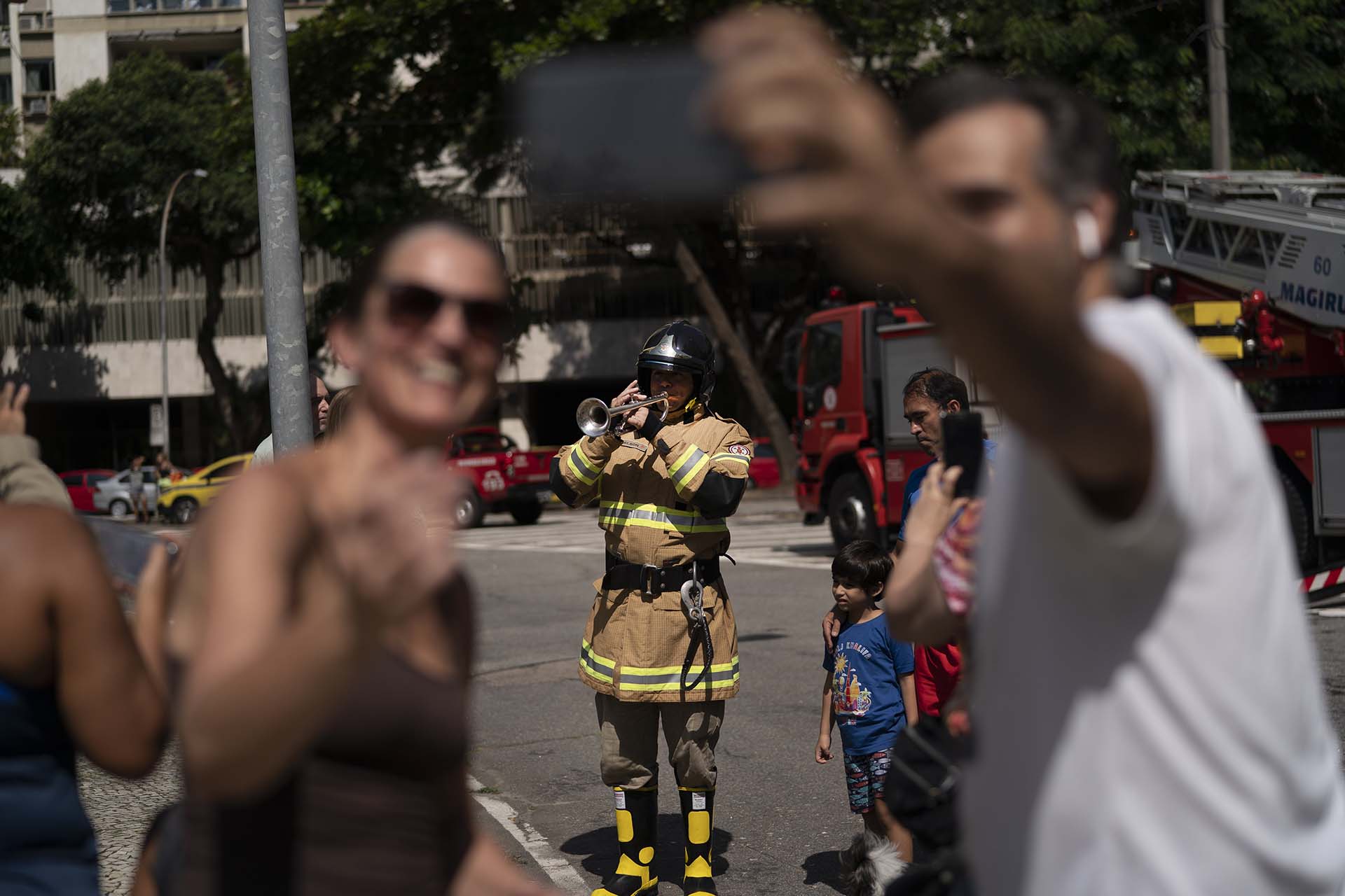 Reisdentes se toman una fotografía con el bombero Elielson Silva mientras éste toca la trompeta, en Río de Janeiro, Brasil (AP Photo/Leo Correa)