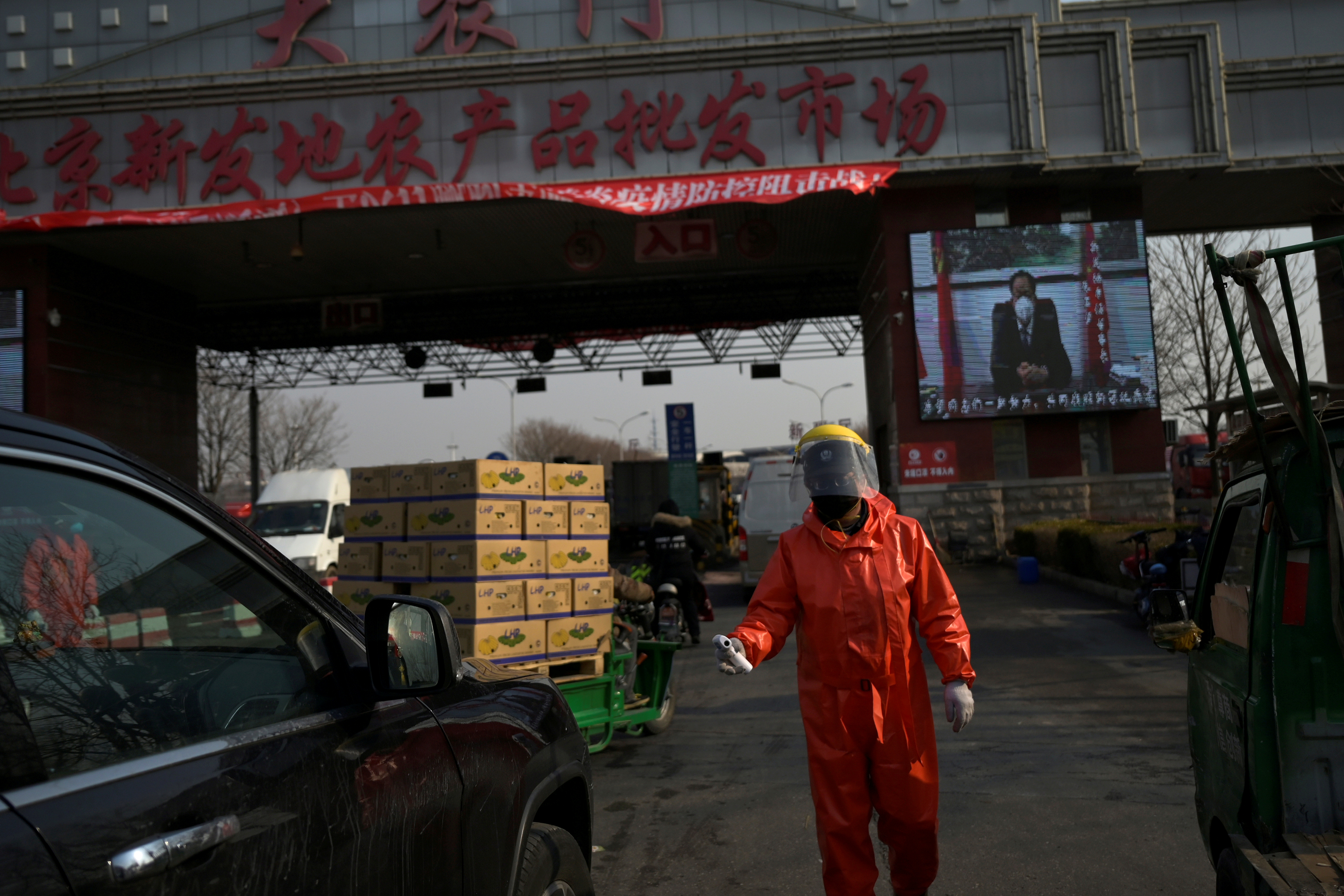 Un trabajador en traje de protección sostiene un termómetro mientras revisa los autos que ingresan al mercado mayorista de Xinfadi (Reuters)