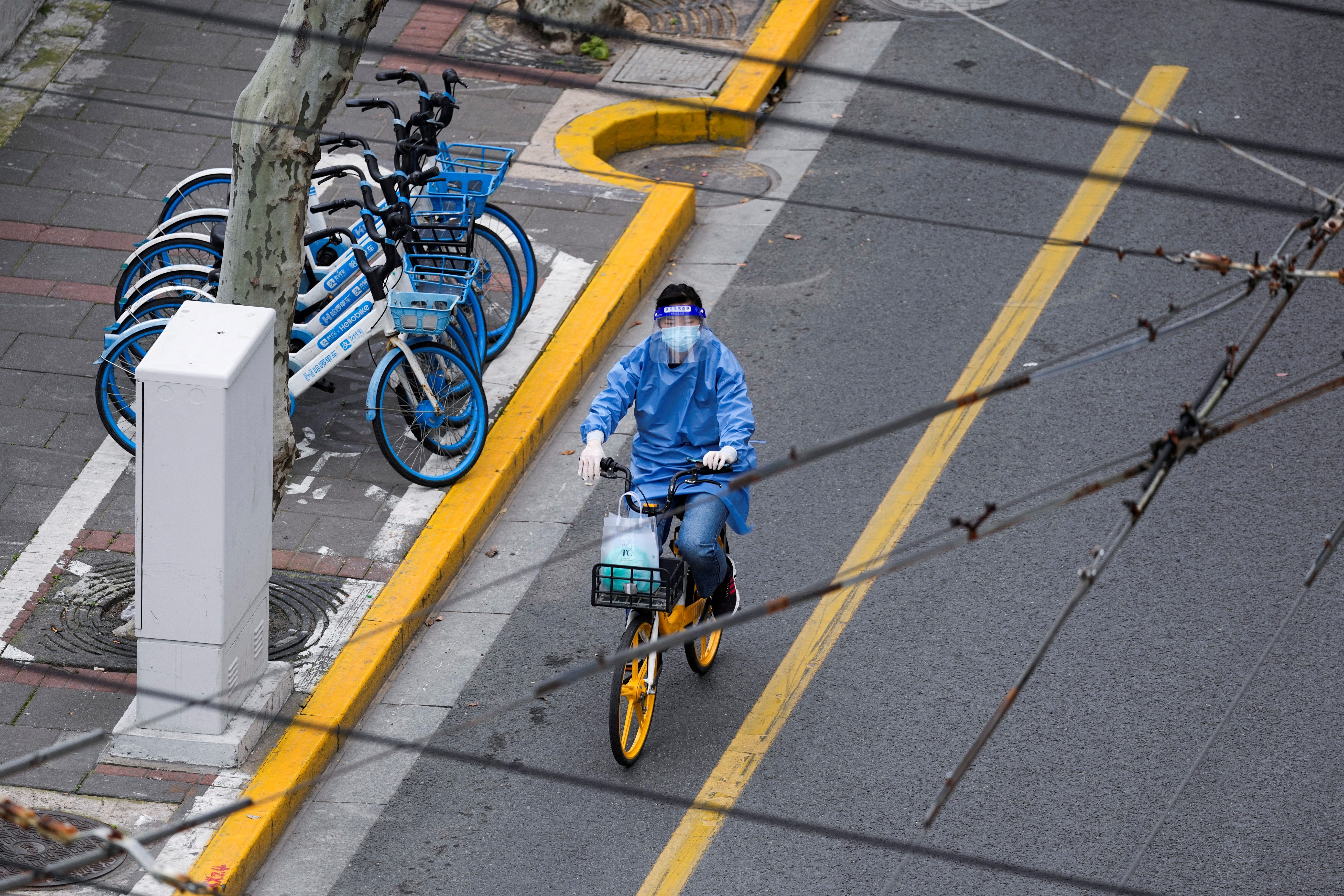 FILE PHOTO: A woman in personal protective equipment (PPE) rides a bicycle on a street, during the lockdown to curb the spread of the coronavirus disease (COVID-19) in Shanghai, China, April 5, 2022. REUTERS/Aly Song/File Photo