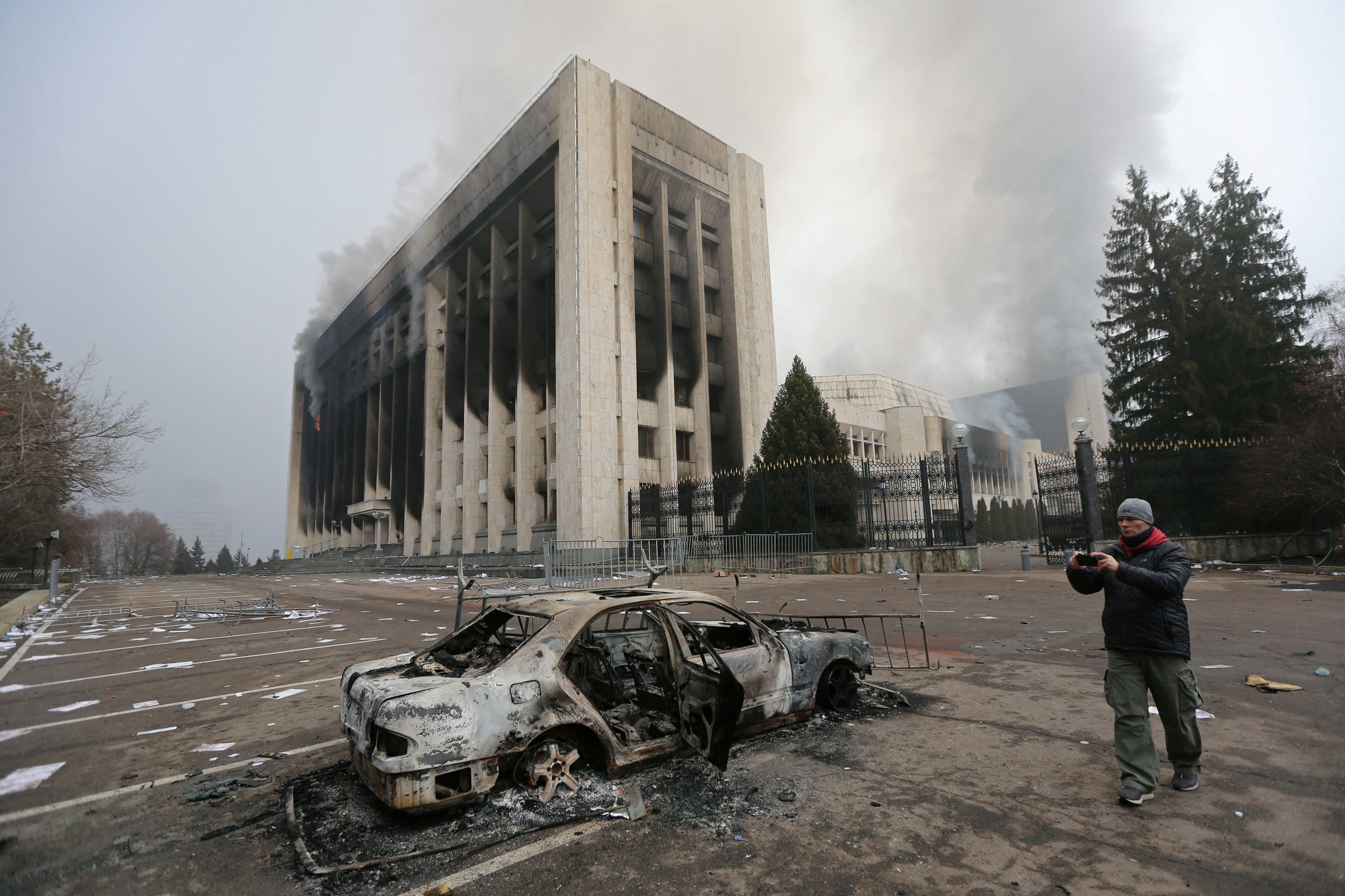 Un hombre toma una foto mientras se ve un coche quemado frente al edificio de la alcaldía que fue incendiado durante las protestas desencadenadas por el aumento del precio del combustible en Almaty, Kazajistán 6 de enero de 2022. REUTERS/Pavel Mikheyev