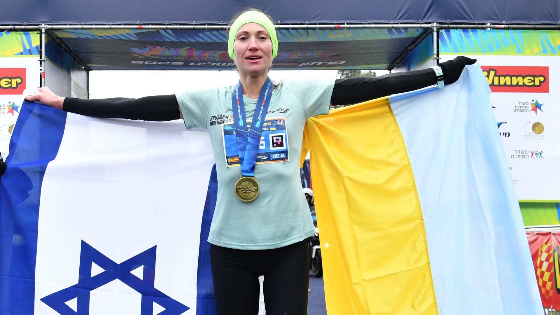 Ukrainian athlete Valentyna Veretska holds the Israeli and Ukranian flags after she won the Jerusalem's International Marathon on March 25, 2022 in Jerusalem. - Veretska, who fled Russia's invasion of her country and took refuge in Israel, won the Jerusalem marathon, race organisers said. The 31-year-old was one of around 40 Ukrainians who took part in the race in Jerusalem's Old City, braving unseasonably cold and wet weather. (Photo by SportsPhotography / Jerusalem's International Marathon / AFP) / == RESTRICTED TO EDITORIAL USE - MANDATORY CREDIT "AFP PHOTO / HO /Jerusalem's International Marathon - NO MARKETING - NO ADVERTISING CAMPAIGNS - DISTRIBUTED AS A SERVICE TO CLIENTS ===
