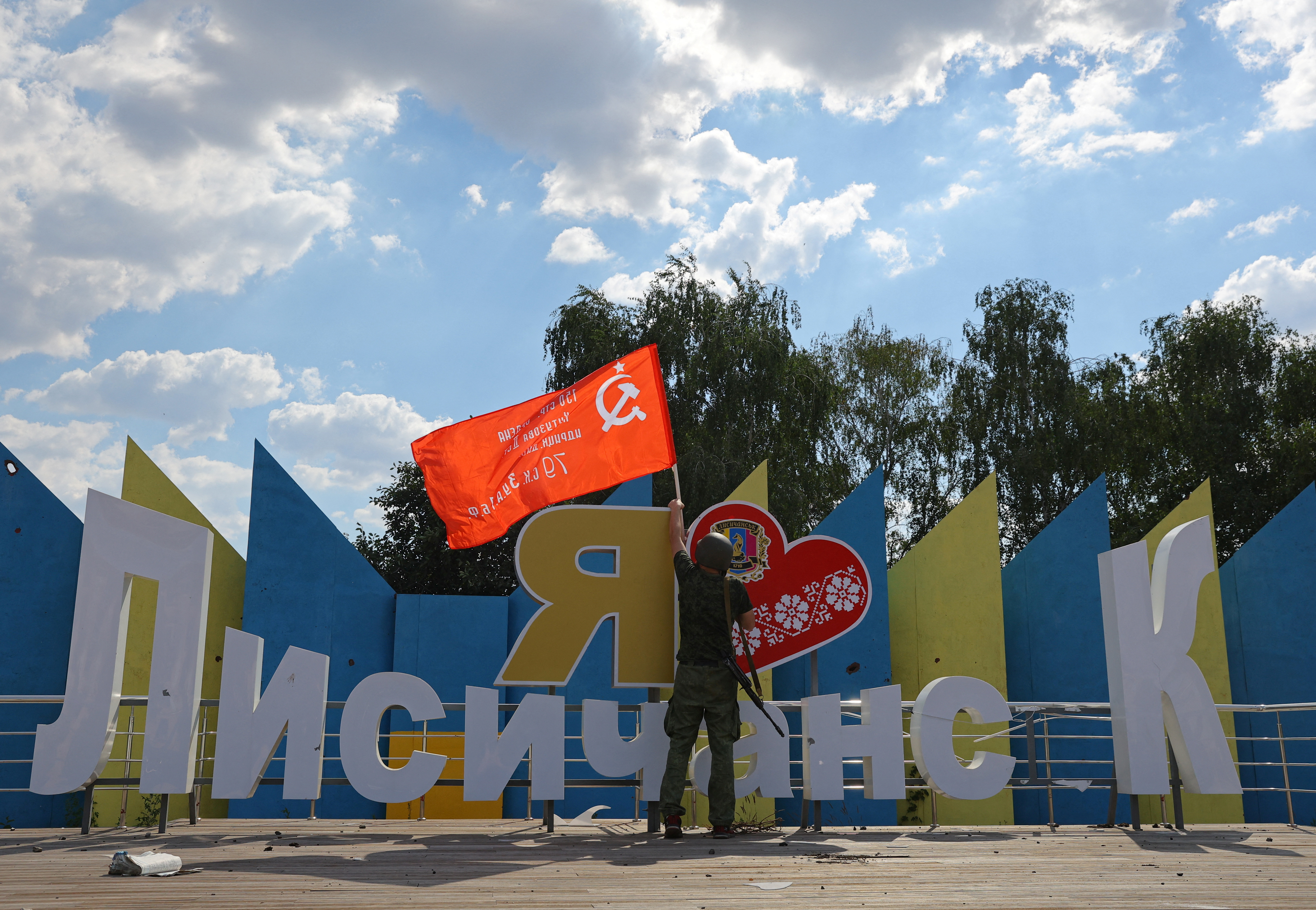 Un miembro de las fuerzas pro-rusas levanta una bandera de la era soviética en el cartel turístico de la entrada de Lysychansk. REUTERS/Alexander Ermochenko