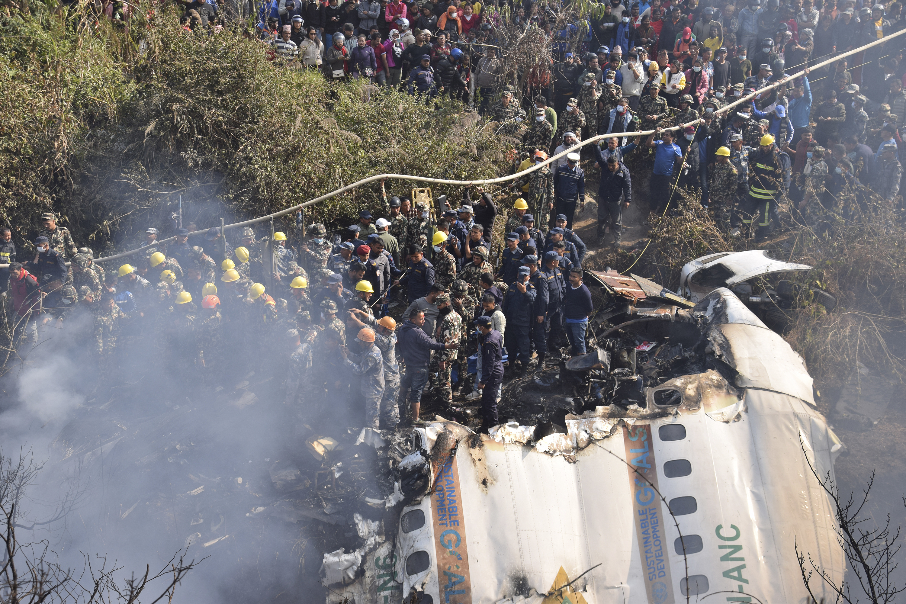 Una multitud observa los restos de un avión de pasajeros accidentado el domingo 15 de enero de 2023, en Pokhara, Nepal. (AP Foto/Krishna Mani Baral)
