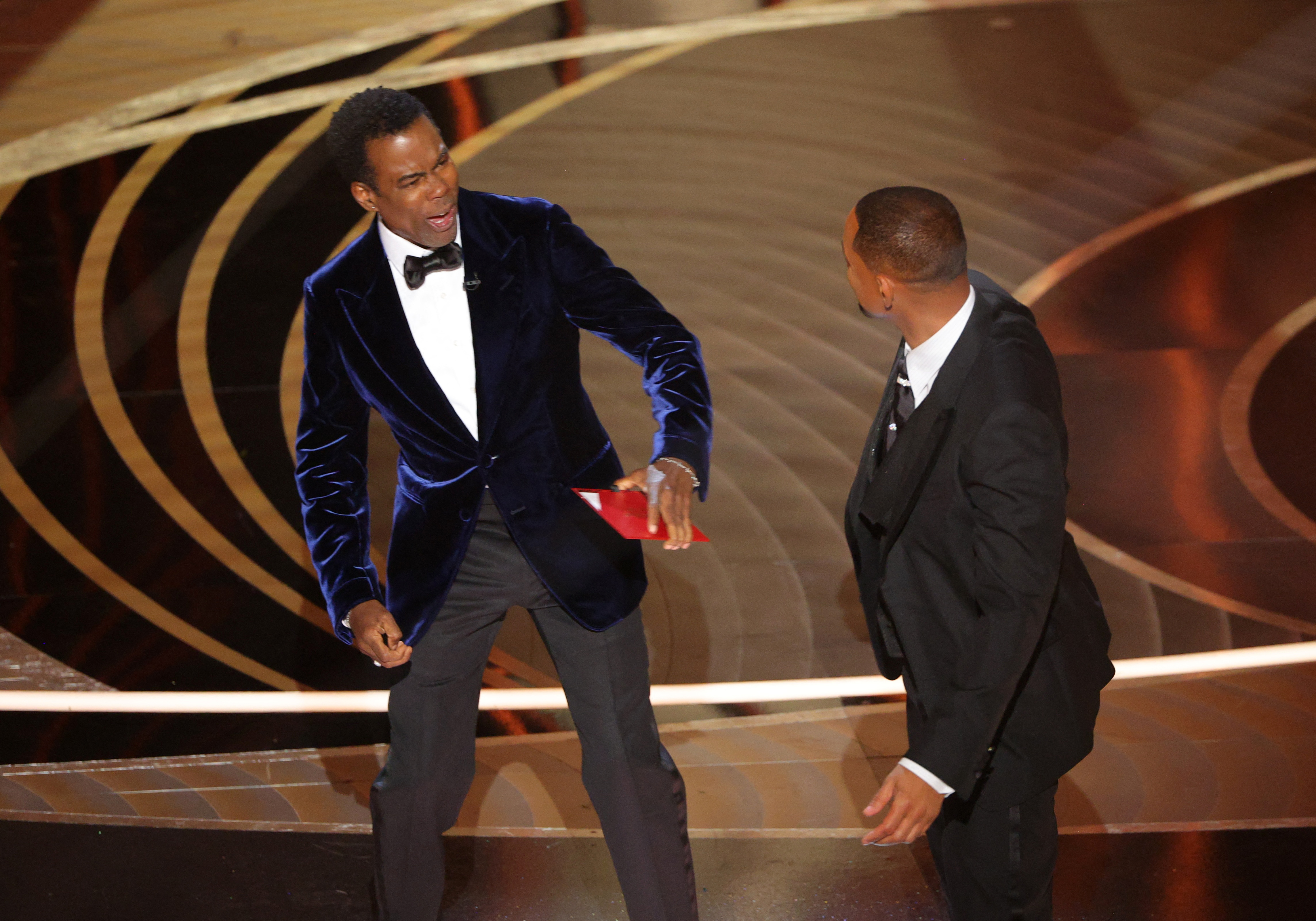 Chris Rock reacts after being hit by Will Smith (R) as Rock spoke on stage during the 94th Academy Awards in Hollywood, Los Angeles, California, U.S., March 27, 2022. REUTERS/Brian Snyder
