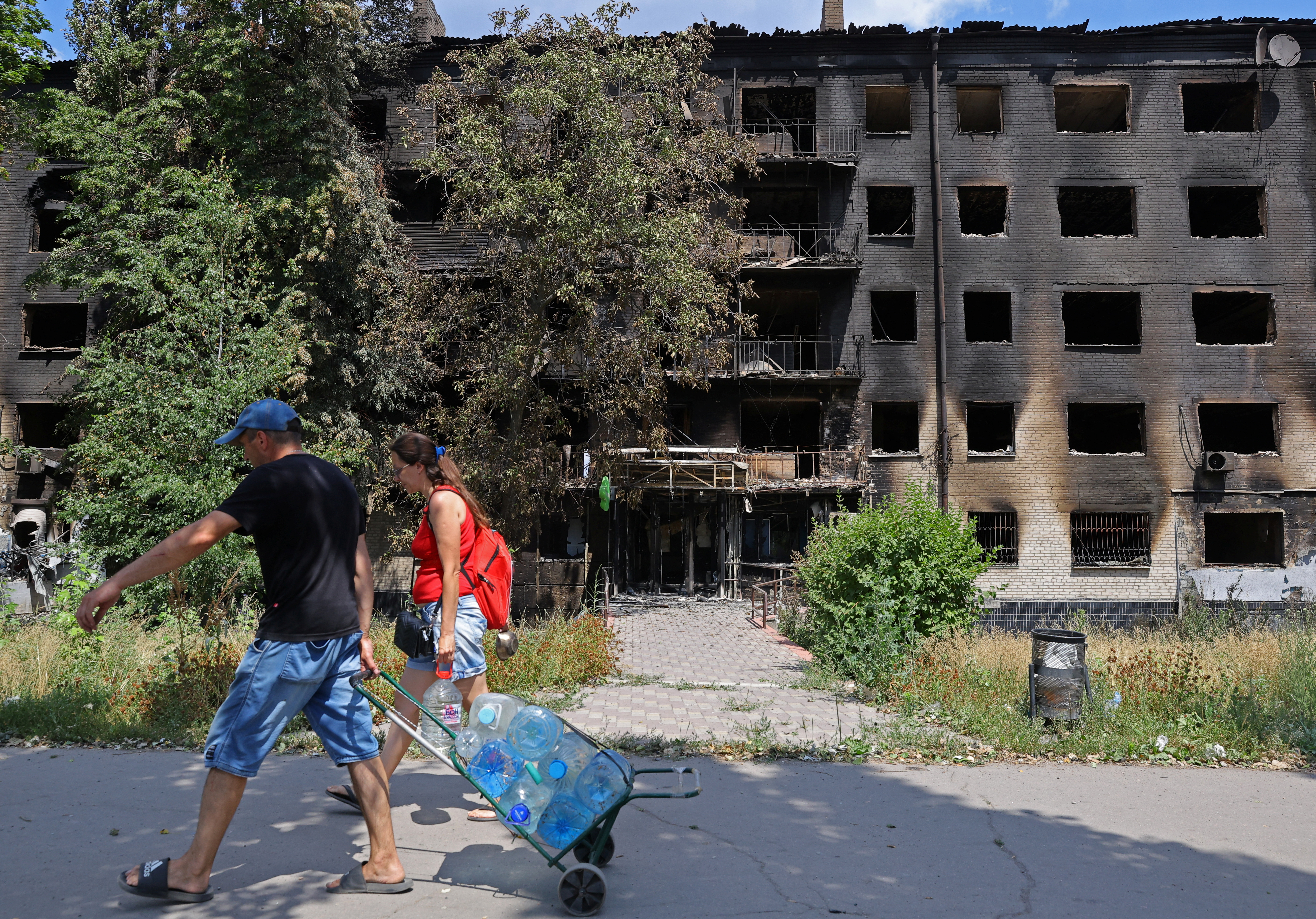 Residentes locales llevan botellas de agua cerca de un edificio destruido en la ciudad de Lisychansk en la región de Luhansk, Ucrania, el 4 de julio de 2022 (Reuters)