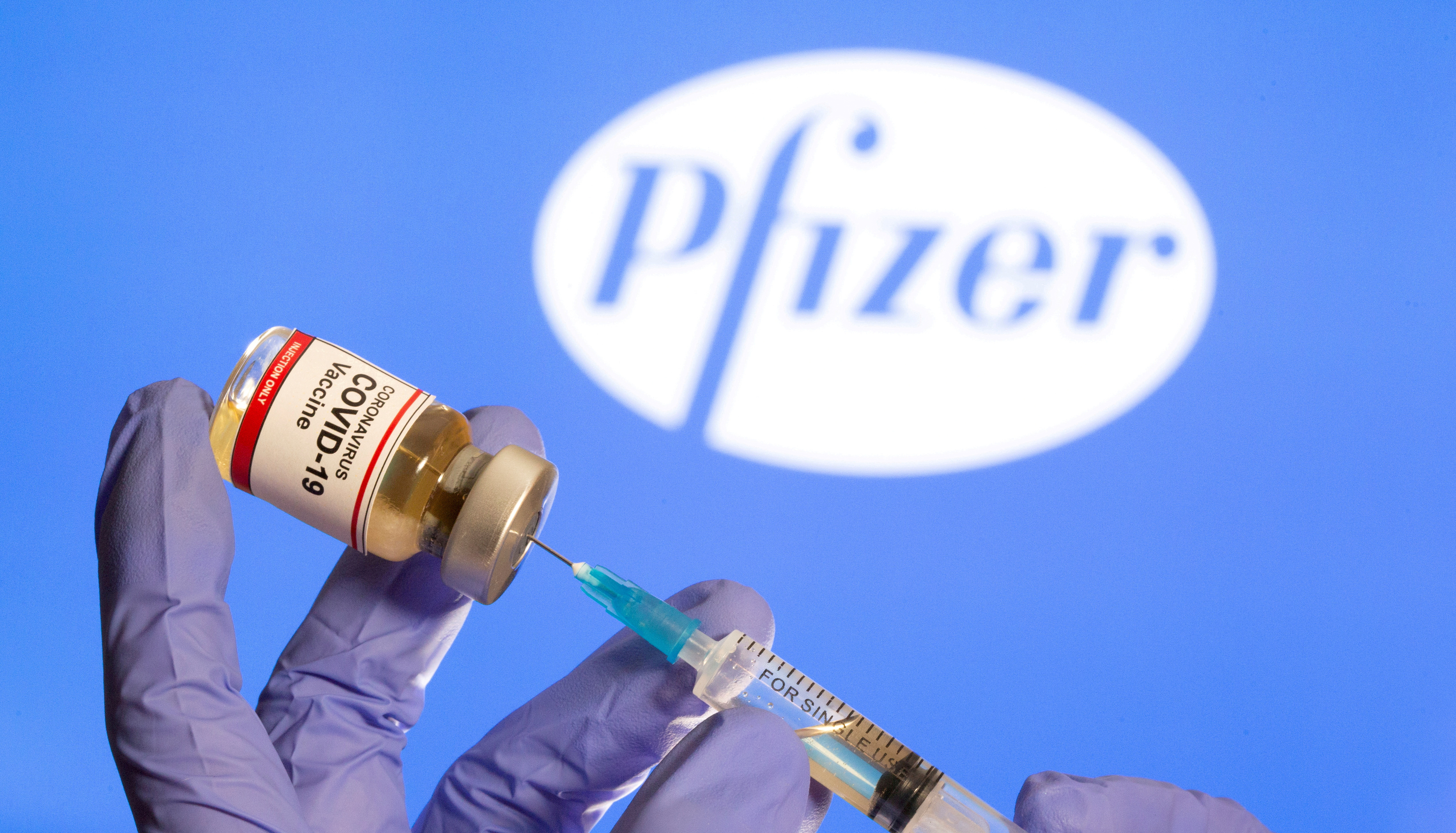 FILE PHOTO: FILE PHOTO: A woman holds a small bottle labeled with a "Coronavirus COVID-19 Vaccine" sticker and a medical syringe in front of displayed Pfizer logo in this illustration taken, October 30, 2020. REUTERS/Dado Ruvic/File Photo/File Photo