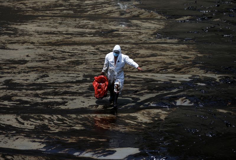 Un trabajador camina tras un derrame de petróleo causado por olas anormales, provocadas por una erupción volcánica submarina masiva a medio mundo de distancia en Tonga, en la playa peruana de Ventanilla, Perú, 18 de enero de 2022. REUTERS/Pilar Olivares