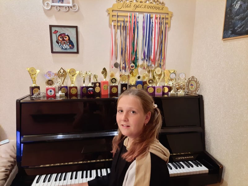 Darinka Monko sentada en su piano junto a las medallas que ha ganado por música, teatro y canto. Adentro, soldados rusos dejaron un artefacto explosivo. Foto: theclaquers