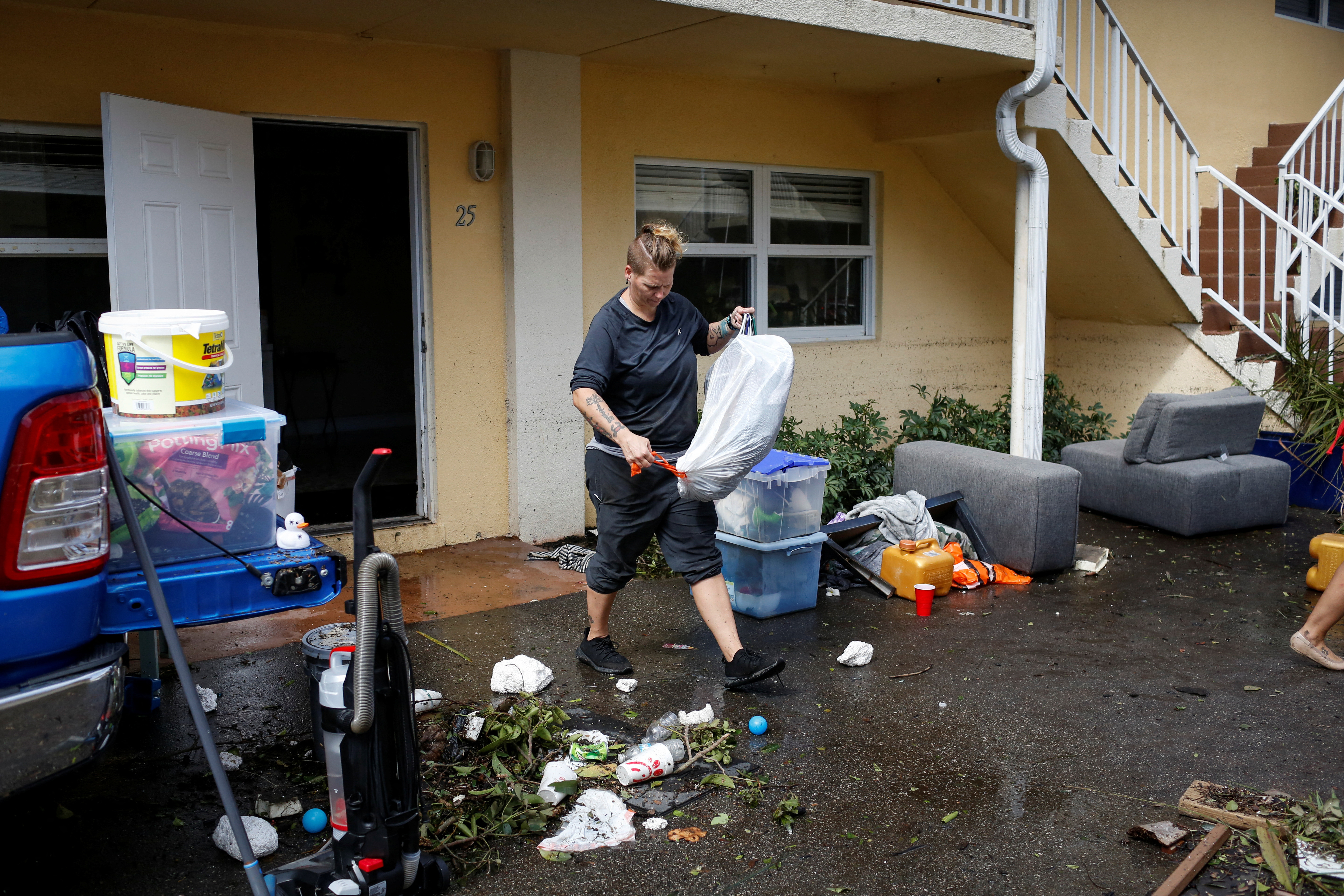 Una mujer lleva ropa en perchas mientras limpia su casa inundada después de que el huracán Ian causara una destrucción generalizada, en Fort Myers, Florida, el 29 de septiembre de 2022. (REUTERS/Marco Bello)