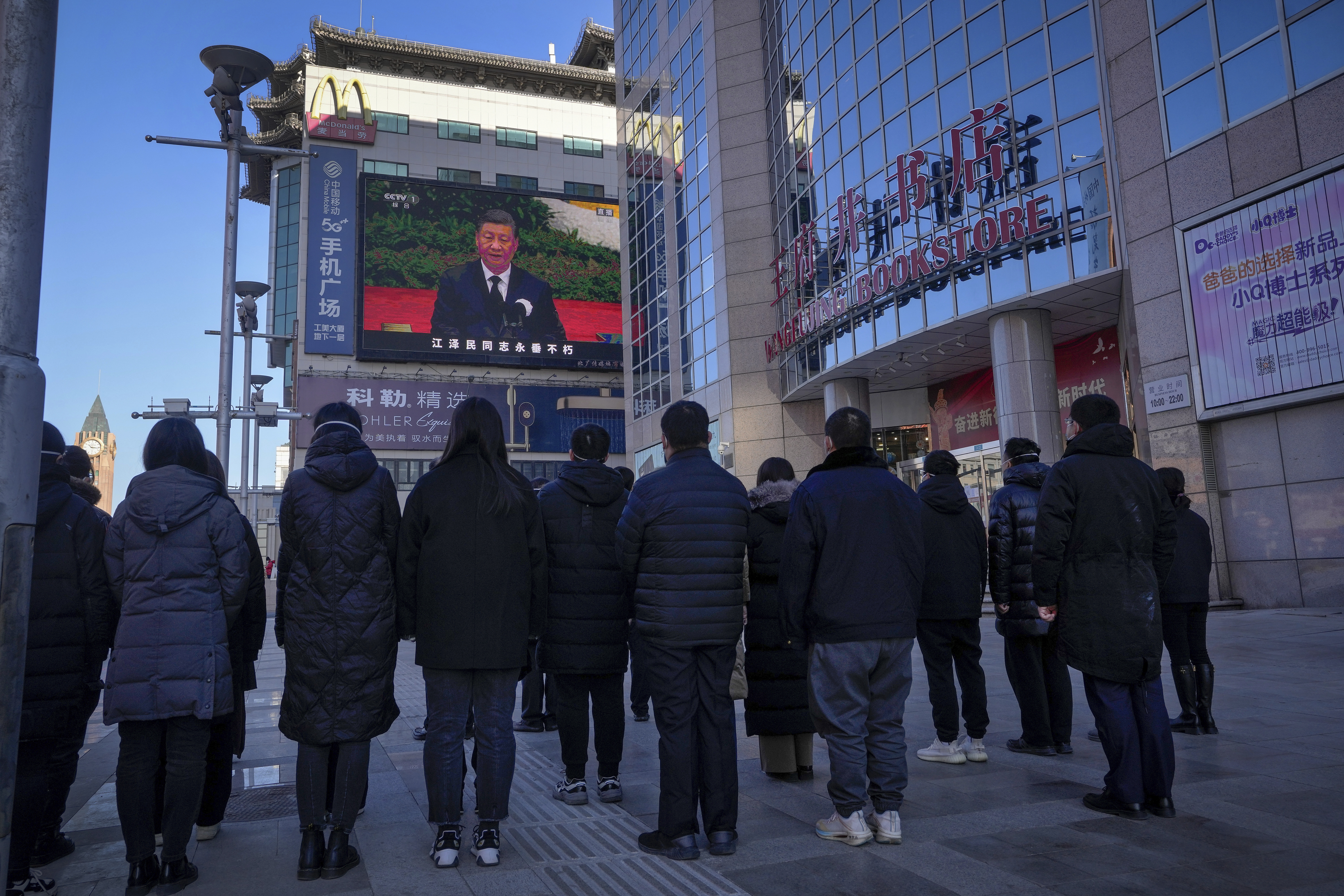Gente mirando una emisión en vivo de un discurso de XI Jinping, en la calle comercial de Wangfujing en Beijing (AP)