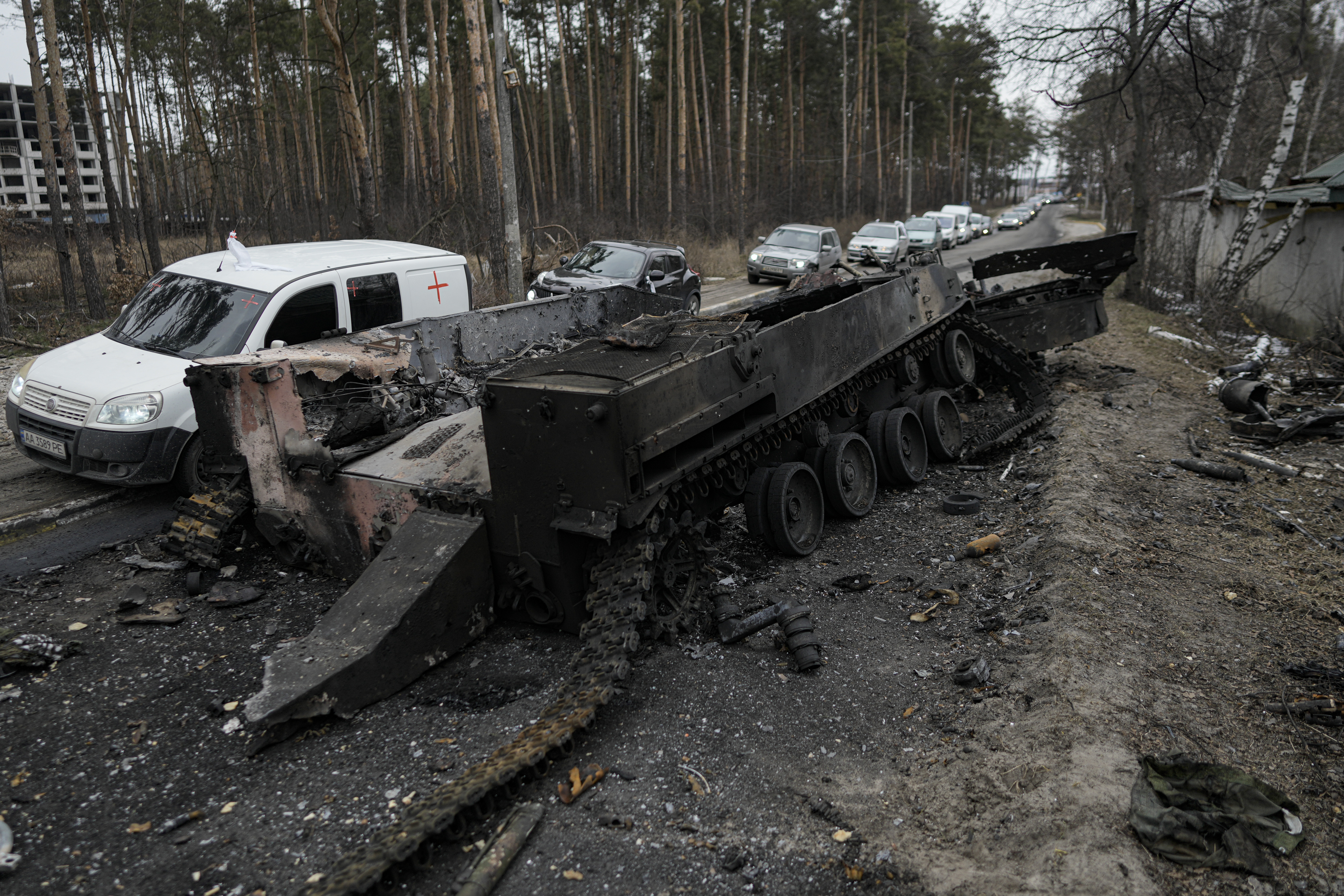 Autos pasan por cerca de un tanque ruso destruido mientras un convoy de vehículos que evacuan a los civiles sale de Irpin, en las afueras de Kiev, Ucrania, el miércoles 9 de marzo de 2022 (AP Photo/Vadim Ghirda)