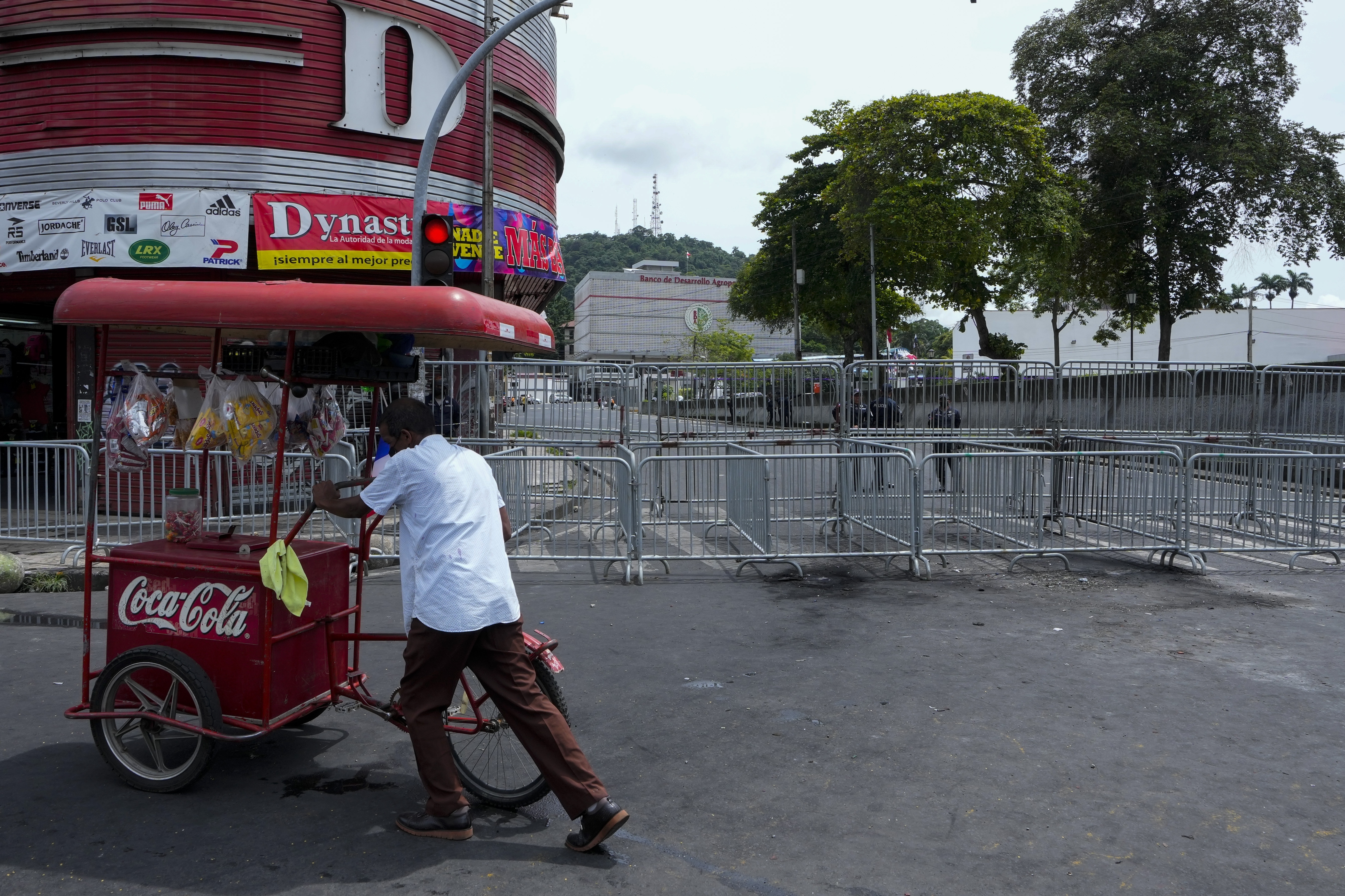 Un vendedor ambulante empuja su carro mientras una huelga de maestros marcha hacia la Plaza 5 de Mayo, cerca de una barricada de seguridad establecida para bloquear el acceso a la Asamblea Nacional en la Ciudad de Panamá, el jueves 14 de julio de 2022. (AP/Arnulfo Franco)