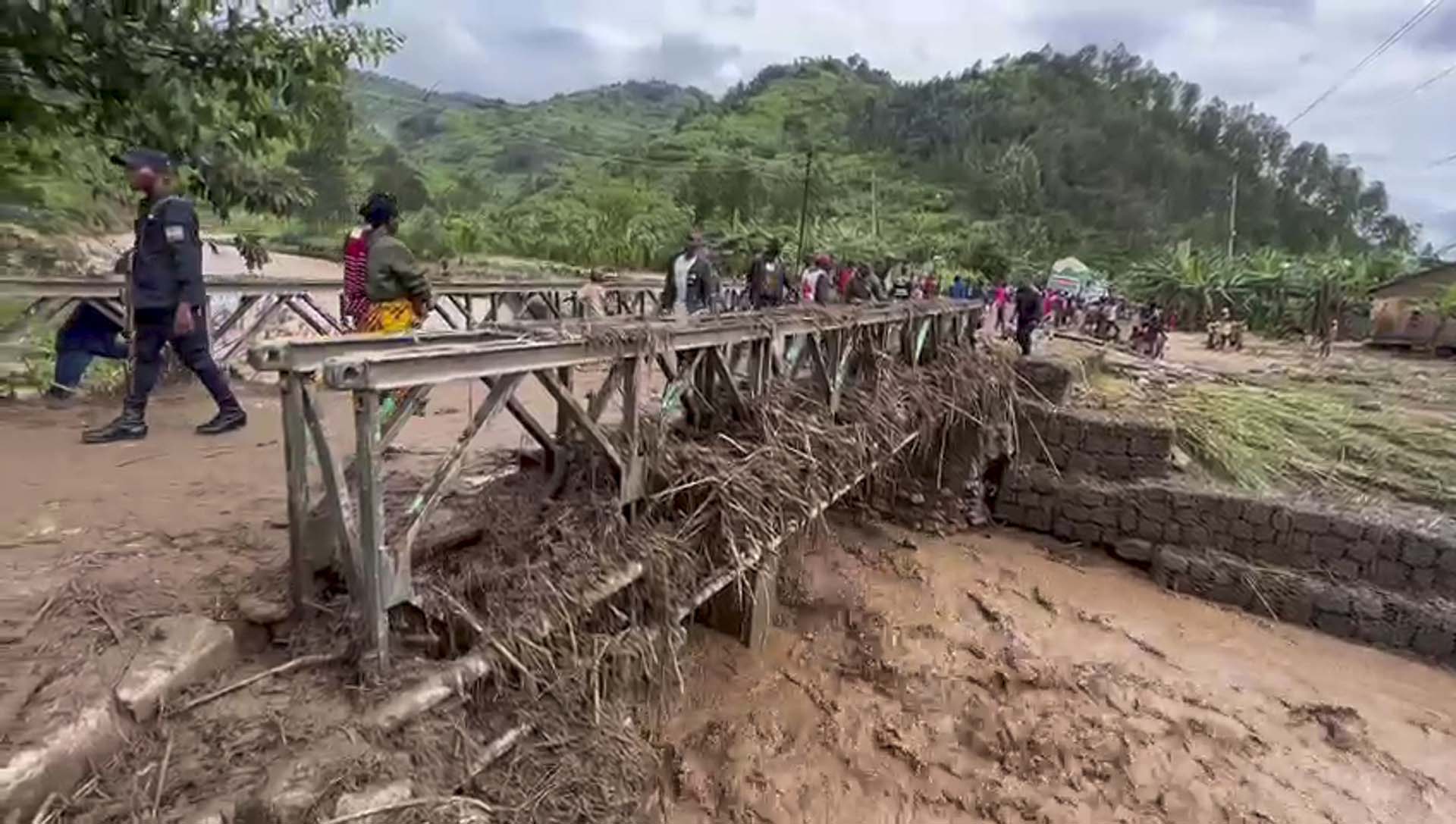 Un grupo de personas cruza un puente sembrado de escombros por las inundaciones  (RwandaTV vía AP)