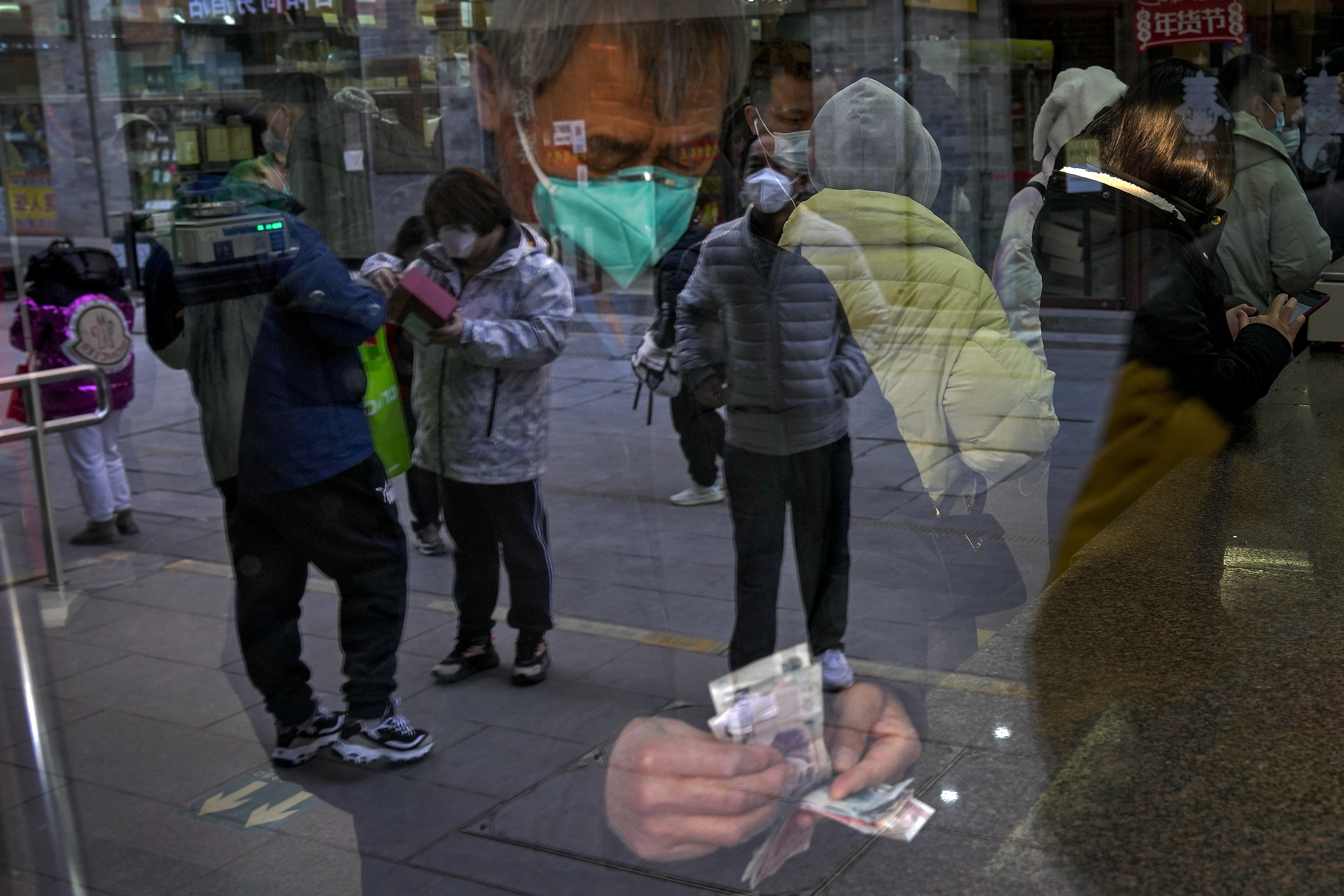 Visitantes se reflejan en el escaparate de una tienda mientras un hombre cuenta billetes en una tienda de venta de té en Qianmen, un conocido lugar turístico de Beijing, el 3 de enero de 2023. (AP Foto/Andy Wong)