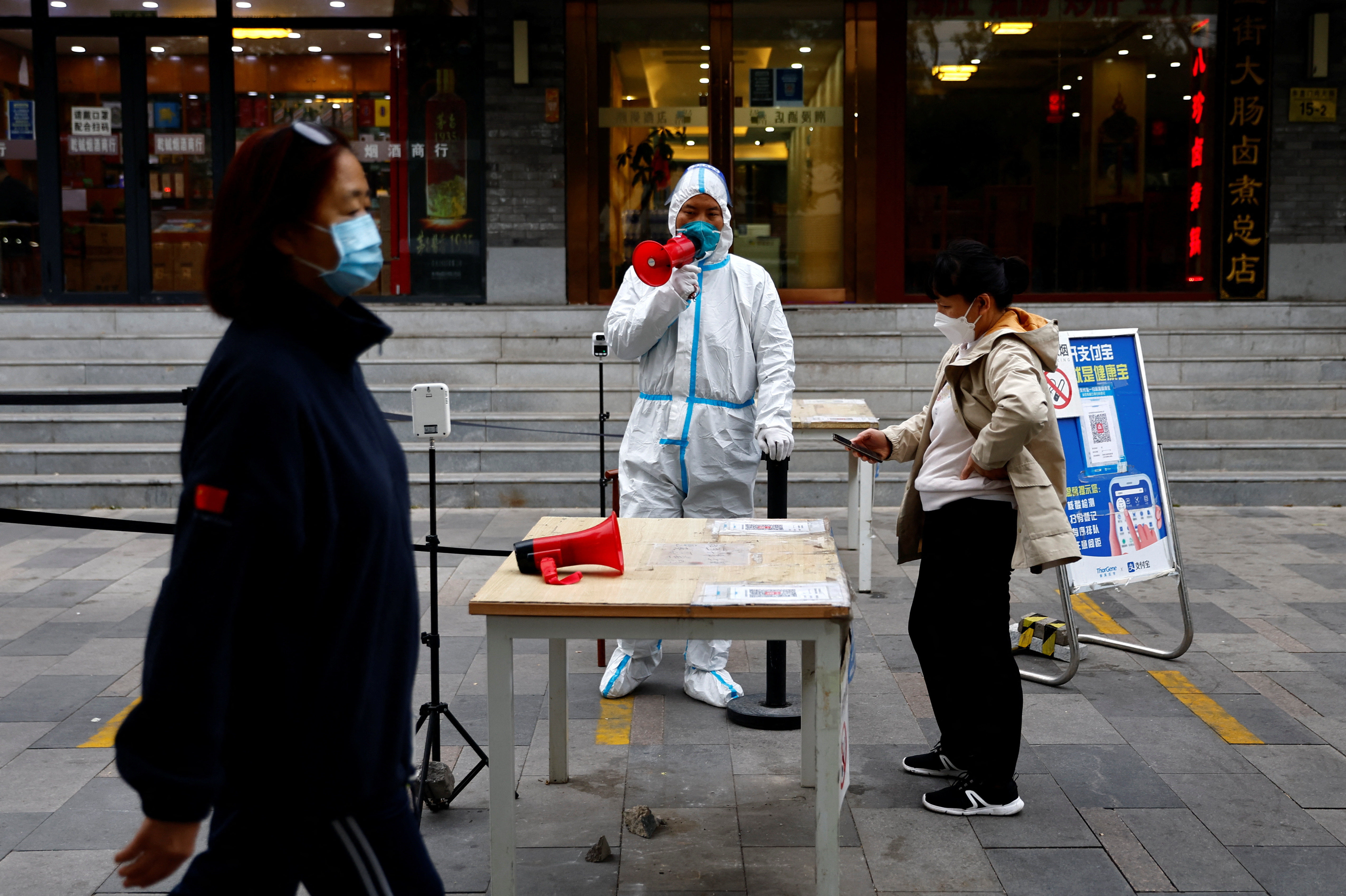 Un trabajador con traje de protección guía a las personas para que escaneen el código sanitario QR antes de someterse a la prueba de la enfermedad del coronavirus (COVID-19) en un puesto de pruebas, en Beijing, China, el 27 de octubre de 2022. REUTERS/Tingshu Wang