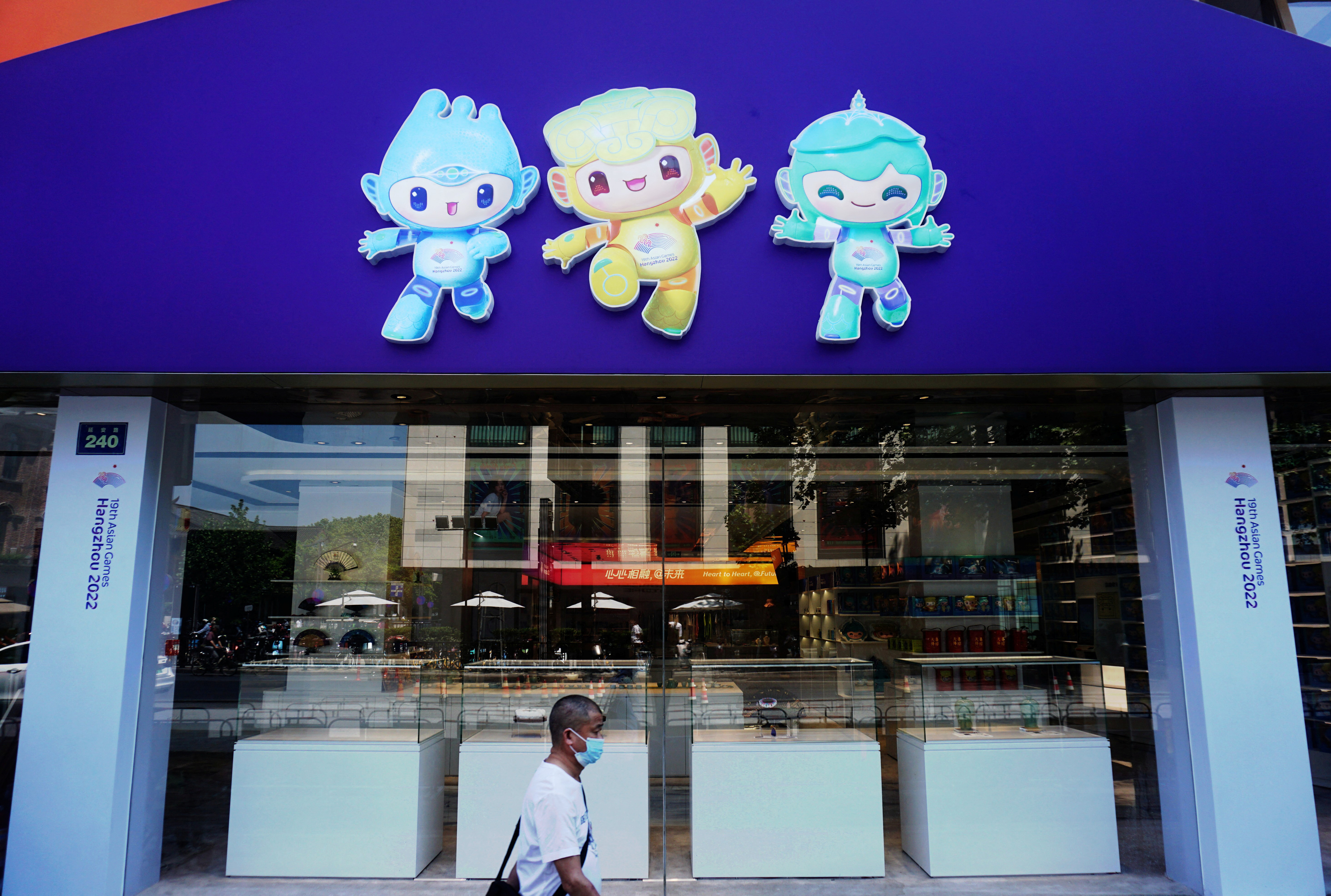 A person wearing a protective mask walks past a souvenir store for the 19th Asian Games Hangzhou 2022, amid the coronavirus disease (COVID-19) outbreak, in Hangzhou, Zhejiang province, China May 6, 2022.  China Daily via REUTERS ATTENTION EDITORS - THIS PICTURE WAS PROVIDED BY A THIRD PARTY. CHINA OUT. NO COMMERCIAL OR EDITORIAL SALES IN CHINA.