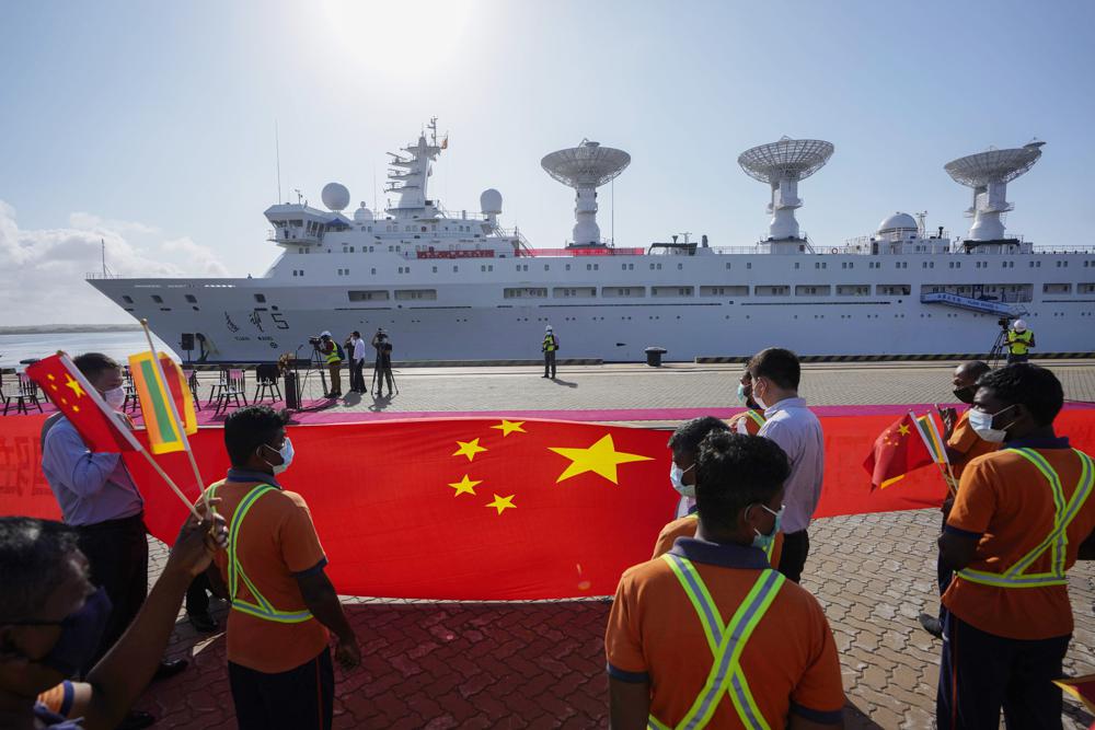 ARCHIVO - Trabajadores portuarios de Sri Lanka sostienen una bandera nacional china para dar la bienvenida al buque de investigación chino Yuan Wang 5, repleto de equipos de vigilancia, a su llegada al puerto internacional de Hambantota, en Hambantota, Sri Lanka, el 16 de agosto de 2022. En 2022, el país entró en suspensión de pagos, incapaz de hacer frente siquiera a los intereses de los préstamos que financiaban la construcción de puertos, carreteras y ferrocarriles. (AP Photo/Eranga Jayawardena)
