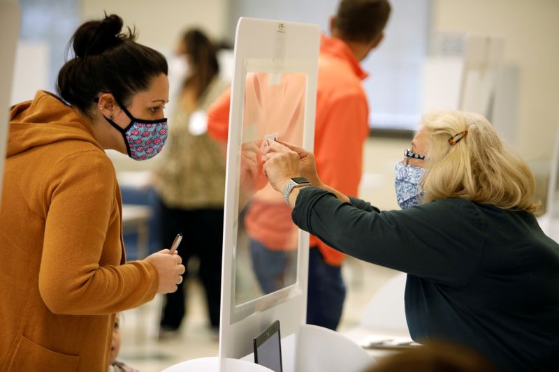 Una trabajadora electoral presenta los detalles de una votante a través de un separador plástico para protegerse del coronavirus en el último día de votación adelantada en persona para las elecciones presidenciales de Estados Unidos en Cornelius, Carolina del Norte, 31 de octubre de 2020 (Reuters/ Jonathan Drake)