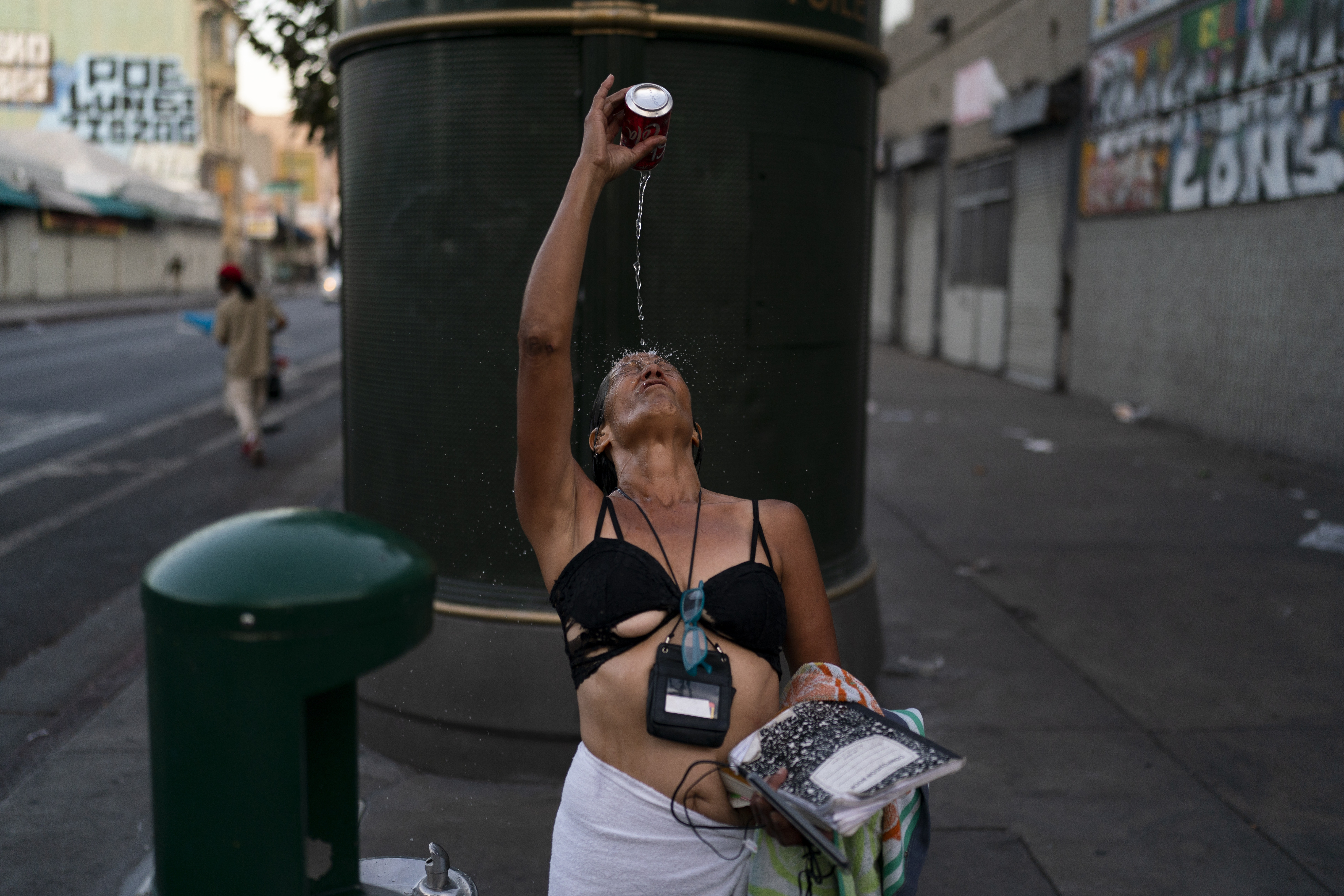 Dolores Flores, una adicta indigente de 57 años, se baña utilizando una lata de refresco que llenó de agua de un bebedero en el área de Skid Row, en Los Ángeles.  (AP Foto/Jae C. Hong)