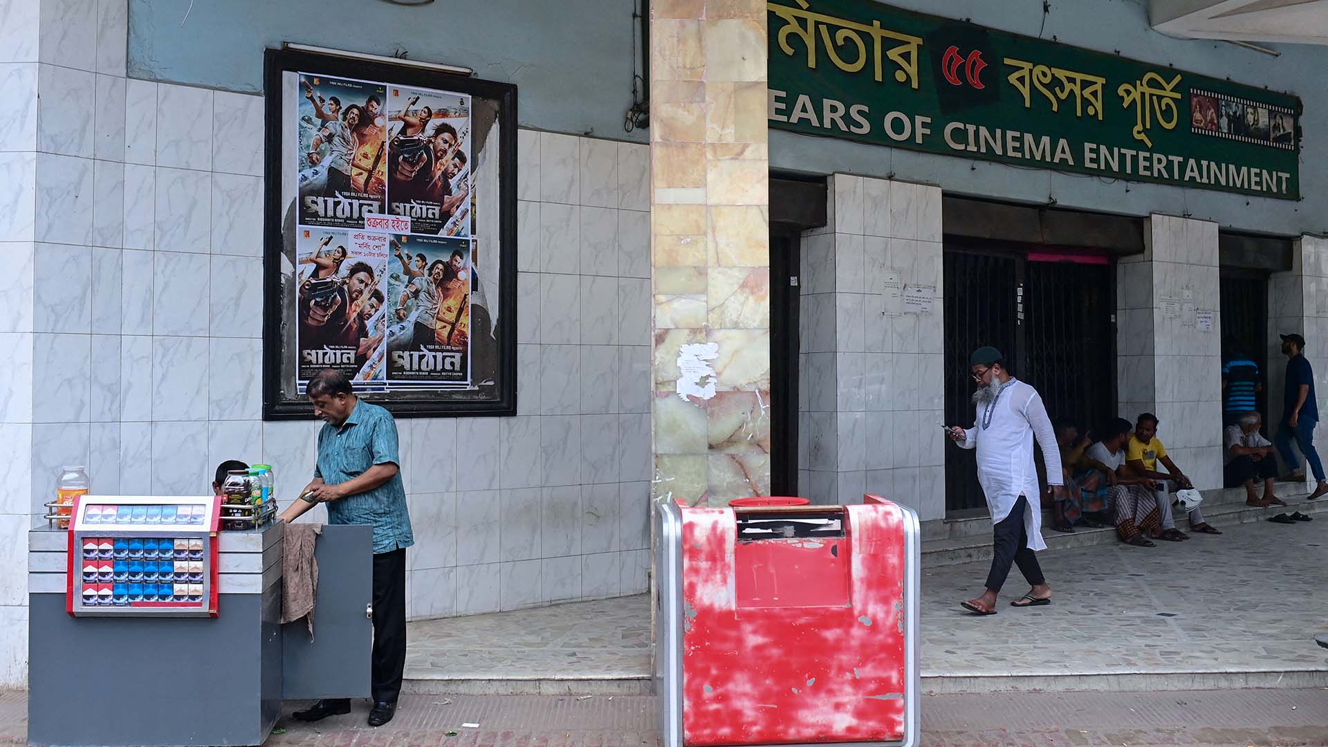People stand next to the posters of the Bollywood film "Pathaan" outside the Modhumita Cinema Hall in Dhaka, on the eve of its release (AFP)