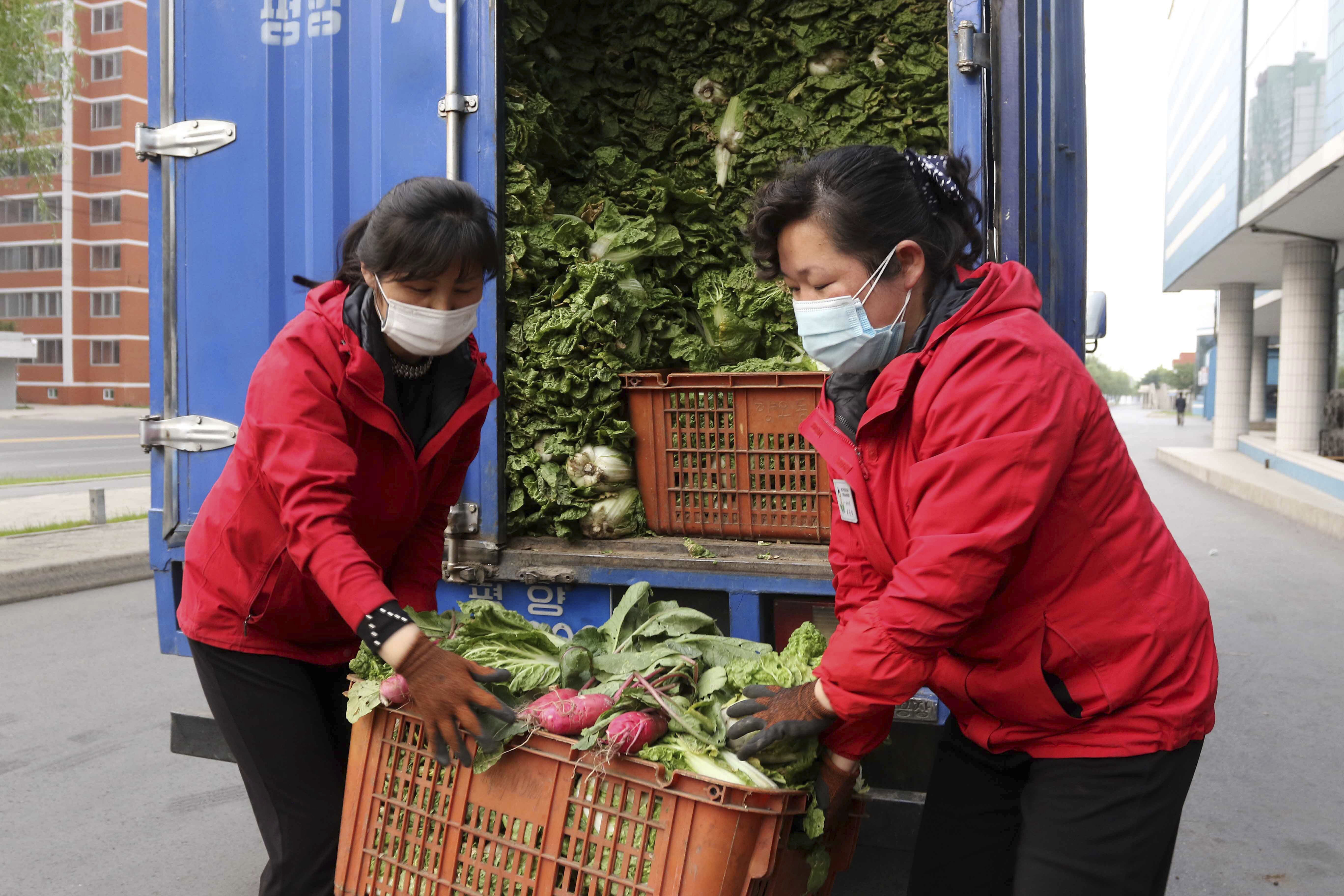 Empleados de una verdulería en la calle de los científicos de Mirae llevan repollos para abastecer a los residentes que se quedan en casa (Foto AP/Jon Chol Jin)