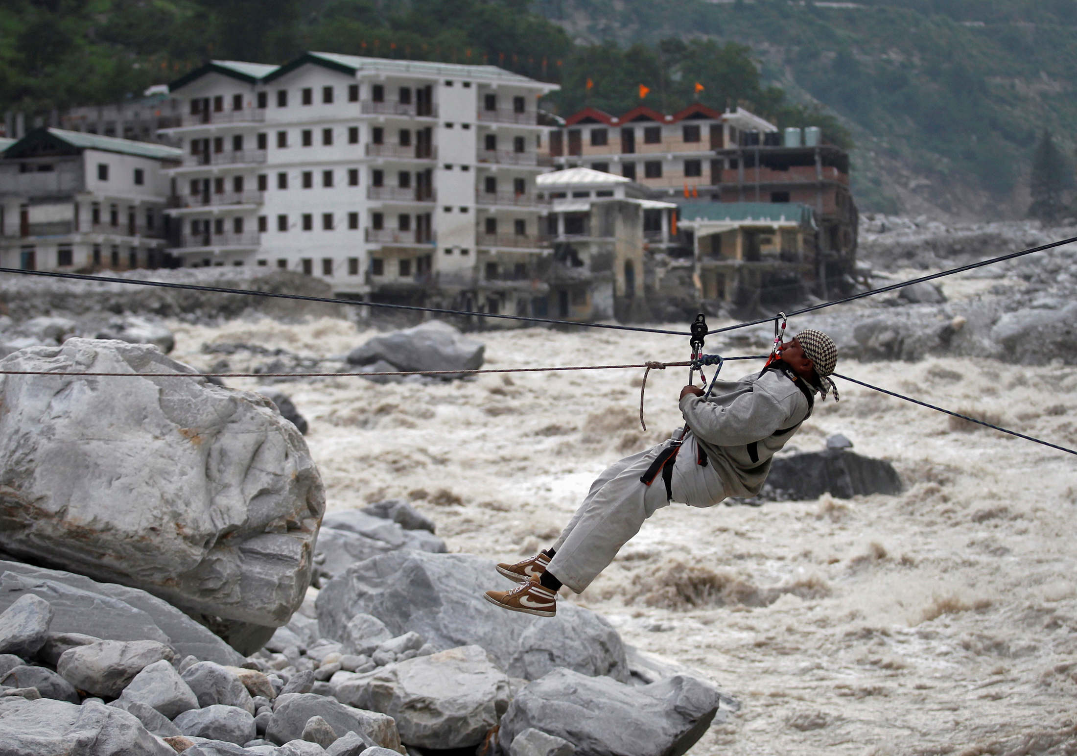 Un hombre es arrastrado a través de una cuerda para ponerse a salvo, mientras se ven los edificios dañados y el río Alaknanda en el fondo, durante una operación de rescate en Govindghat en el estado himalayo de Uttarakhand el 23 de junio de 2013.