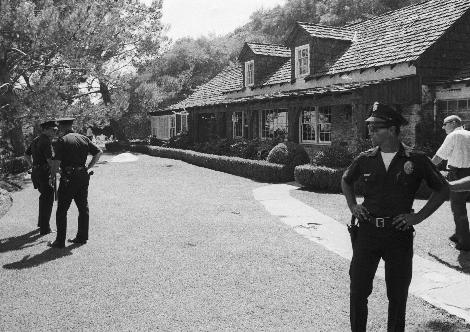 La escena del crimen en Los Ángeles, California: La policía custodia la propiedad alquilada por $200,000 del director de cine Roman Polanski después de que su esposa, la actriz Sharon Tate, y otras cuatro personas fueran encontradas muertas el 9 de agosto de 1969. En el fondo se ve un cuerpo cubierto por una mortaja (Bettmann Archive)
