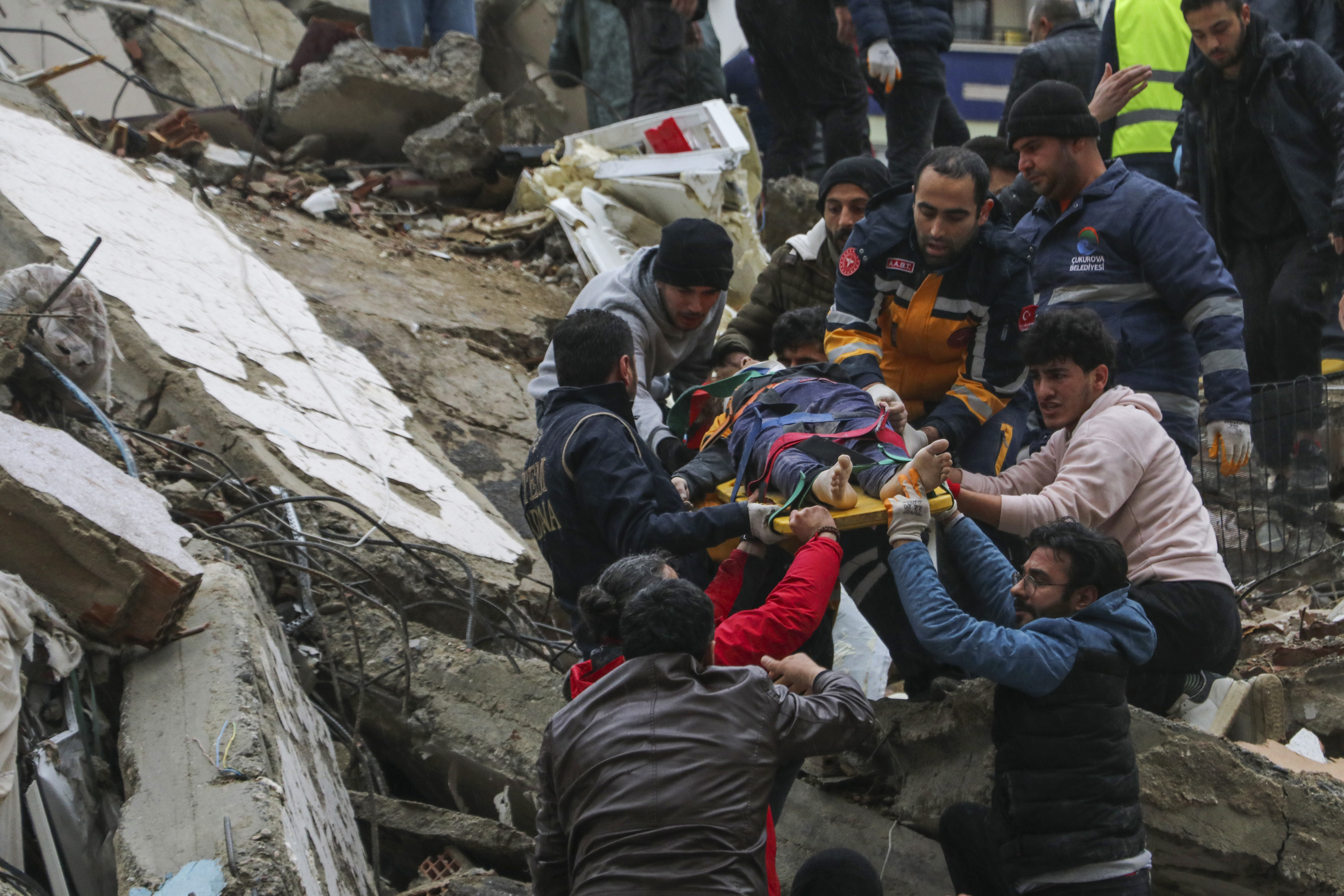 Gente y equipos de rescatistas trasladan a una persona en camilla desde un edificio derruido en Adana, Turquía, el lunes 6 de febrero de 2023. (IHA agency via AP)