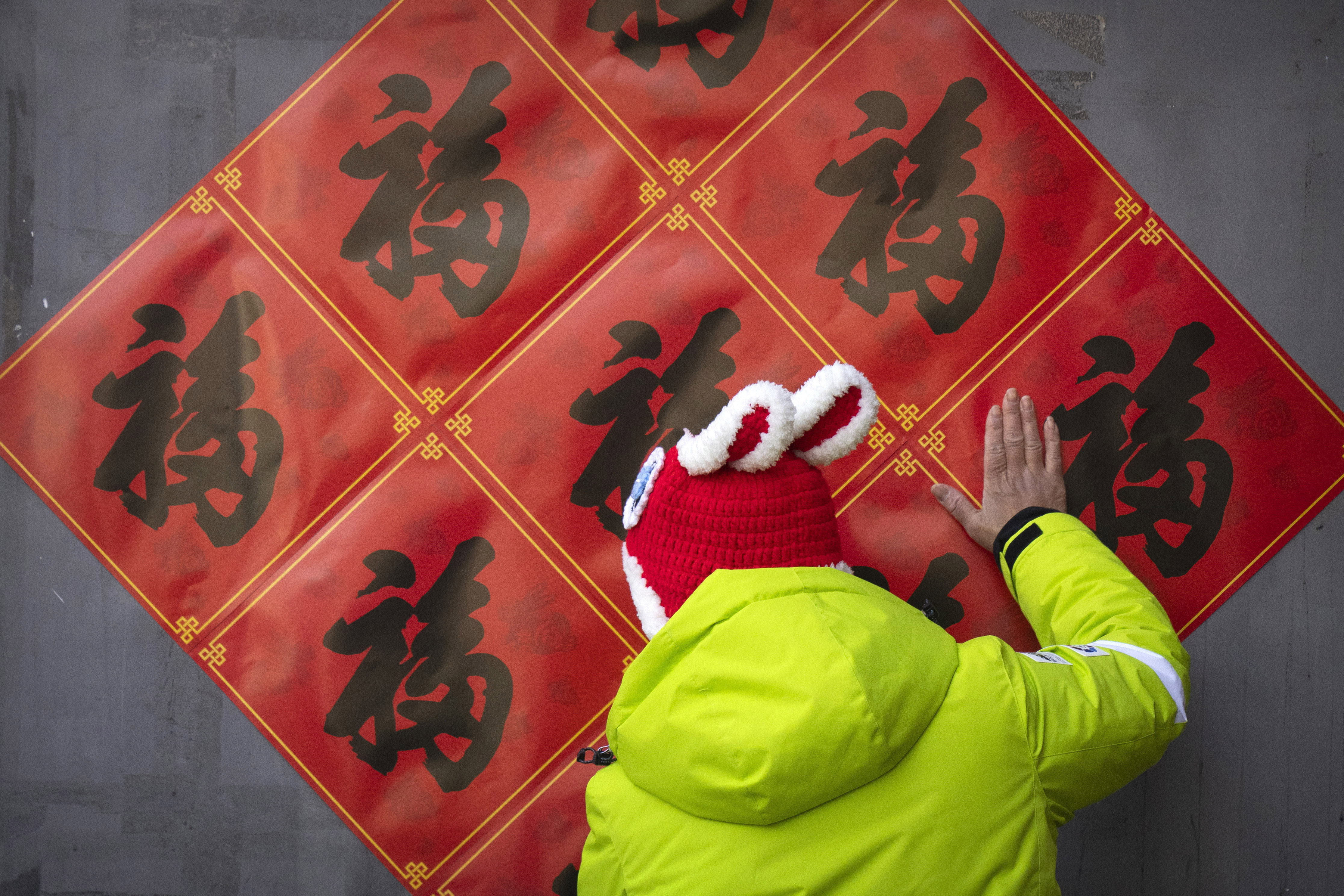 A woman uses her hand to place Lunar New Year decorations on a wall in a shopping street in Beijing, Saturday, Jan. 21, 2023. The Year of the Rabbit officially begins on Sunday.  (AP Photo/Mark Schiefelbein)