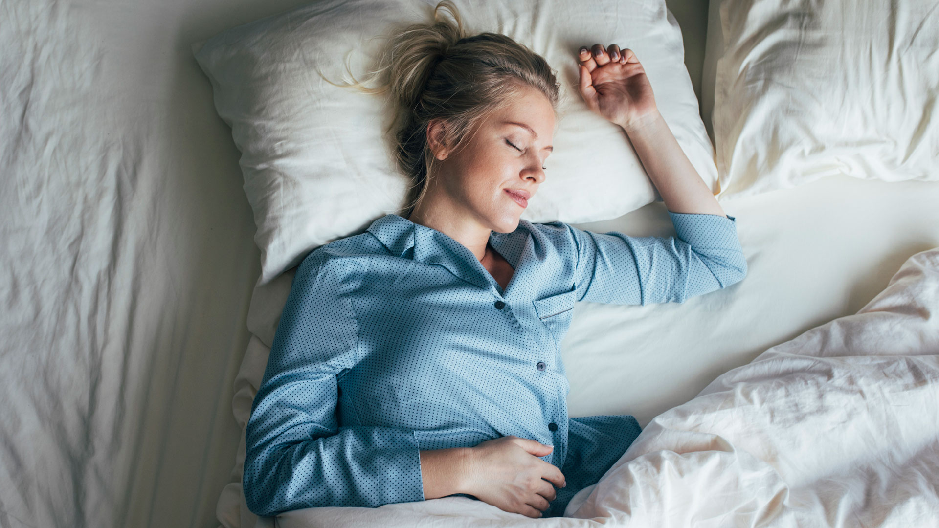 Beautiful happy Caucasian woman in blue pyjamas sleeping on a king-size bed. (Getty)