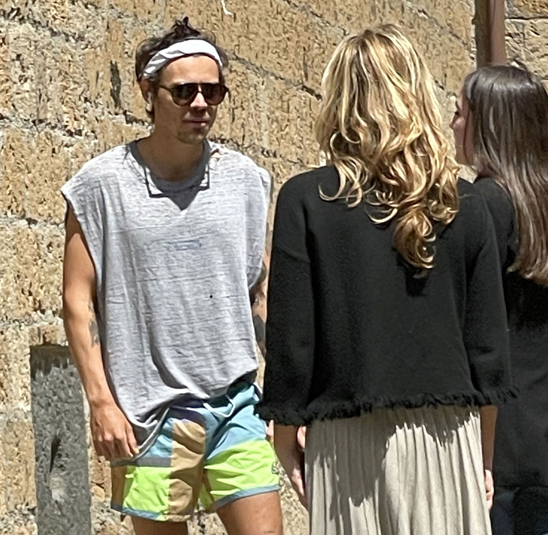 Harry Styles was out walking the streets of Italy, where he is vacationing with Olivia Wilde, and stopped to say hello to a group of fans who recognized him.  He was playing sports, wearing multicolored shorts, gray tank tops, a headband and sunglasses.