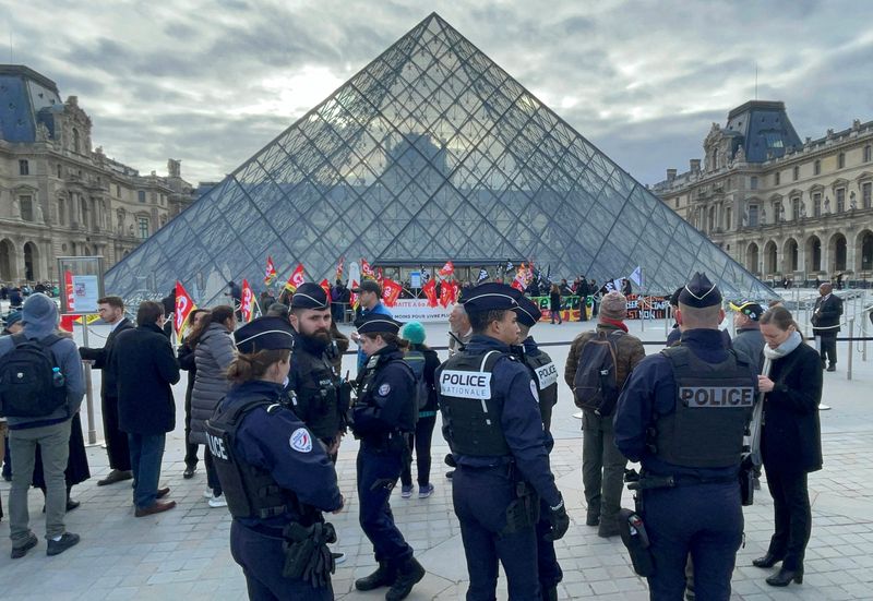La policía francesa mira mientras los manifestantes que sostienen banderas del sindicato francés CGT frente a la Pirámide de cristal del museo del Louvre bloquean la entrada del museo del Louvre para protestar contra la reforma de las pensiones del gobierno francés, en París, Francia, 27 de marzo de 2023.  REUTERS/Marco Trujillo