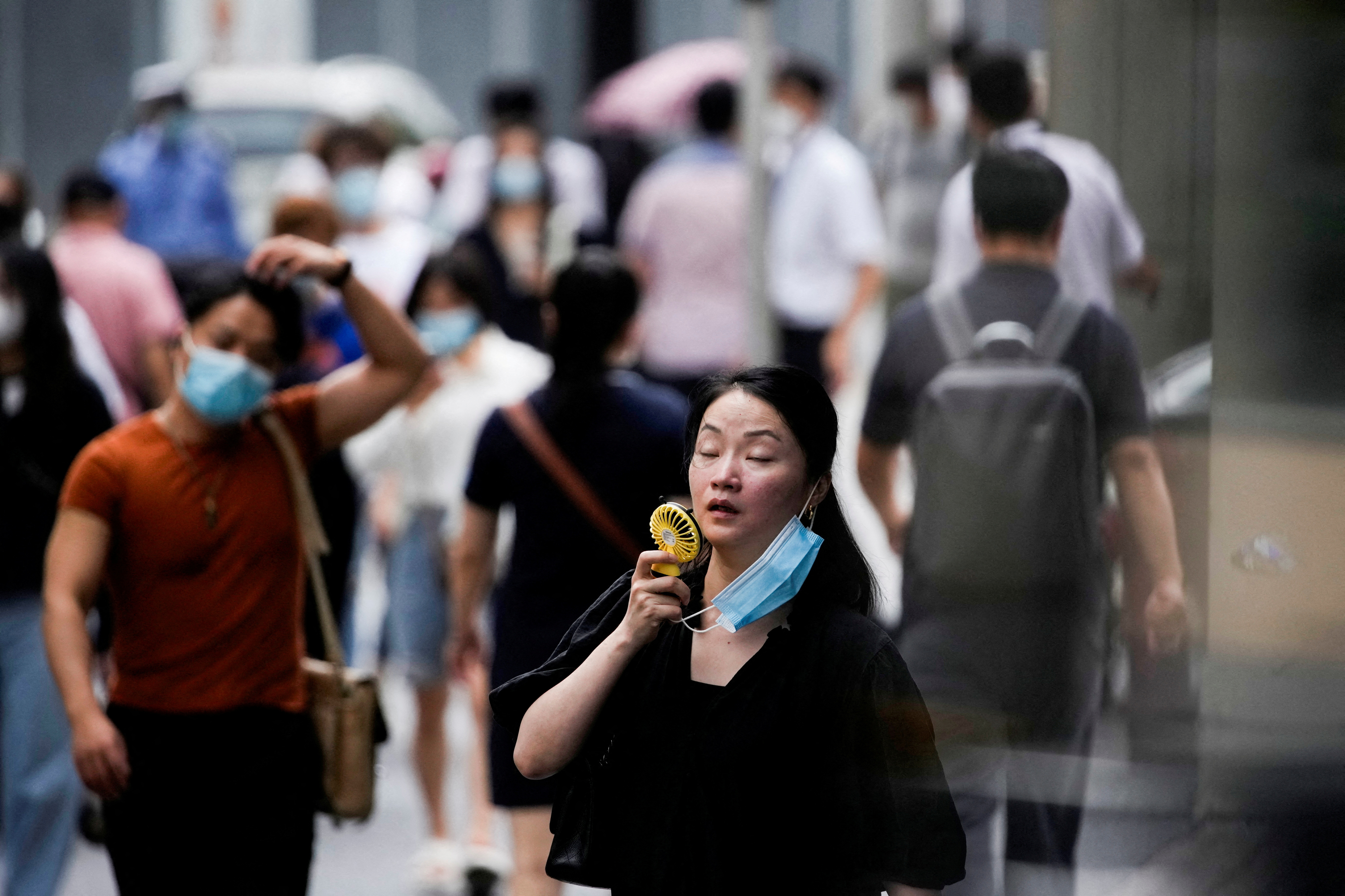 FOTO DE ARCHIVO: Una mujer con mascarilla utiliza un abanico mientras camina por una calle en un día caluroso en Shanghái, China el 19 de julio de 2022. REUTERS/Aly Song