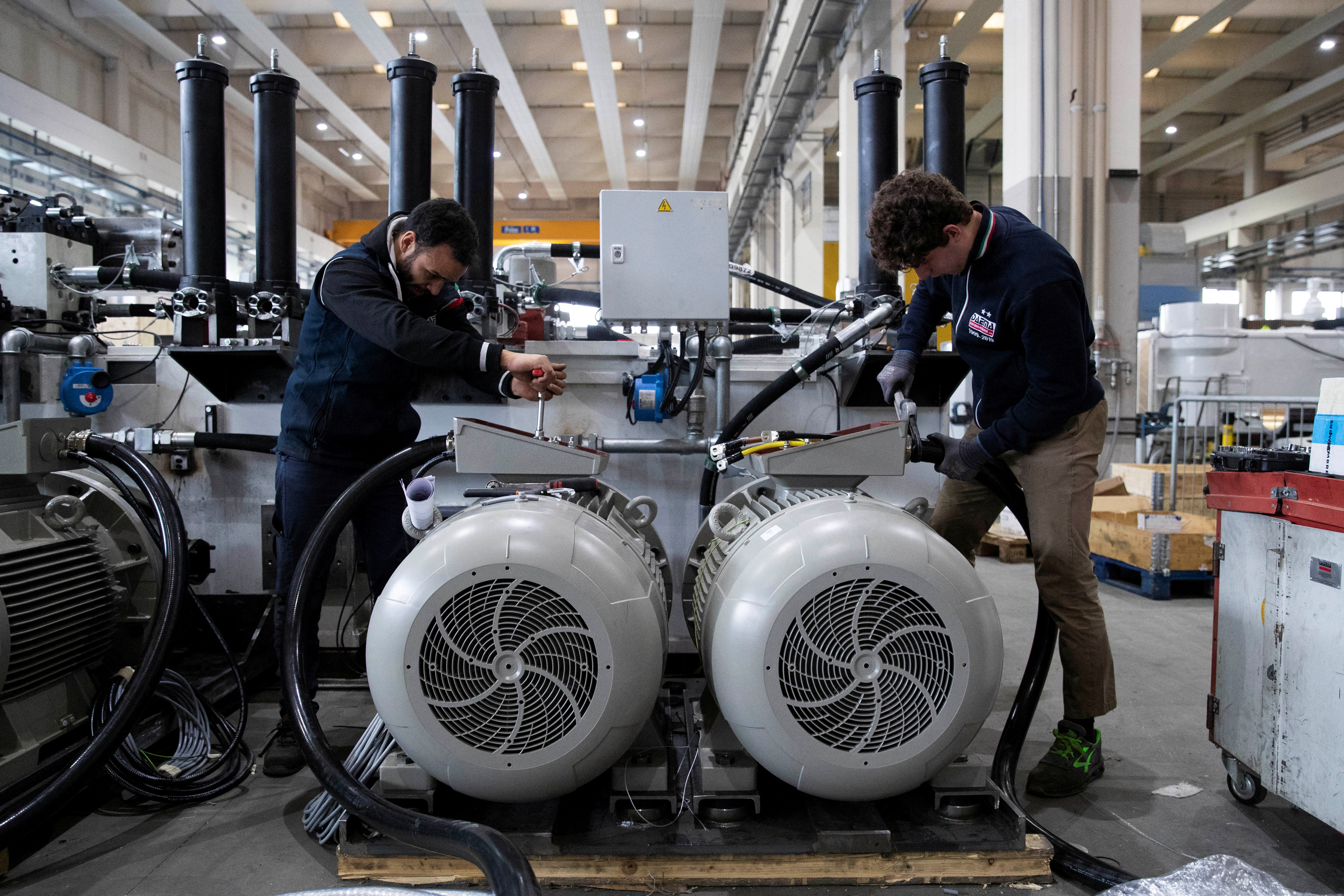 Personas trabajan en piezas de máquinas de prensado en la planta del grupo IDRA en Travagliato, norte de Italia, 25 de enero de 2023. (REUTERS/Alessandro Garofalo)