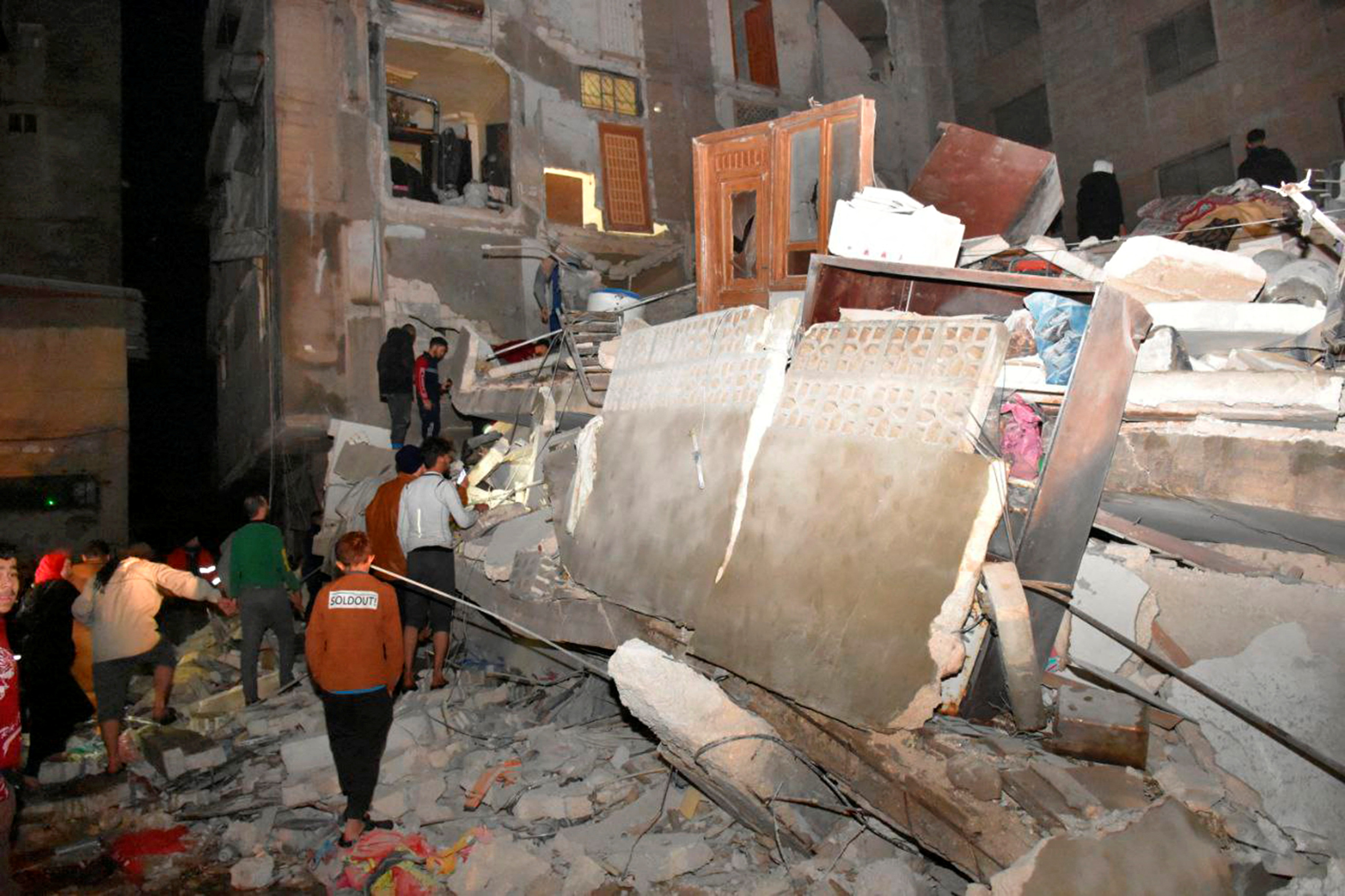 Las personas se reúnen en el sitio de un edificio derrumbado, luego de un terremoto, en Hama, Siria.
