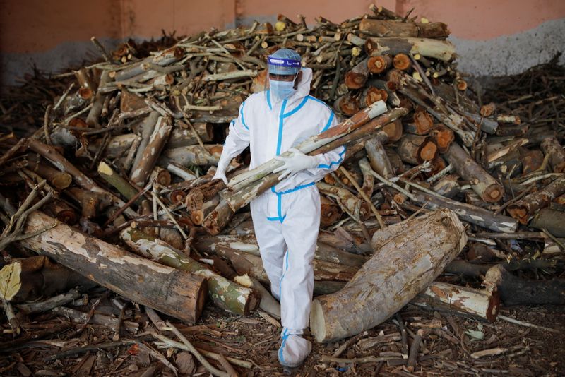 Un hombre con un equipo de protección individual (EPI) transporta madera para prearar una pira funeraria para fallecidos por la COVID-19 en un crematorio en Nueva Dehli, la India, el 26 de abril de 2021. REUTERS/Adnan Abidi