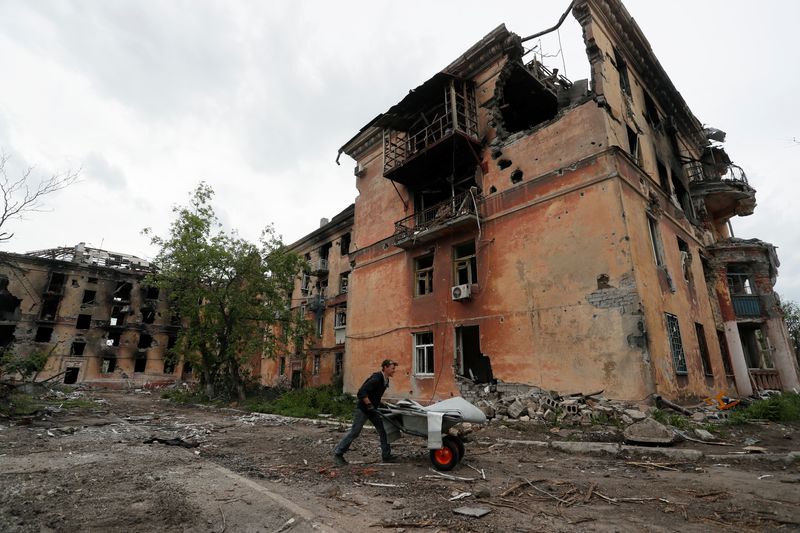 Un residente local empuja una carretilla frente a un edificio de apartamentos fuertemente dañado en Mariúpol (Foto: Reuters)