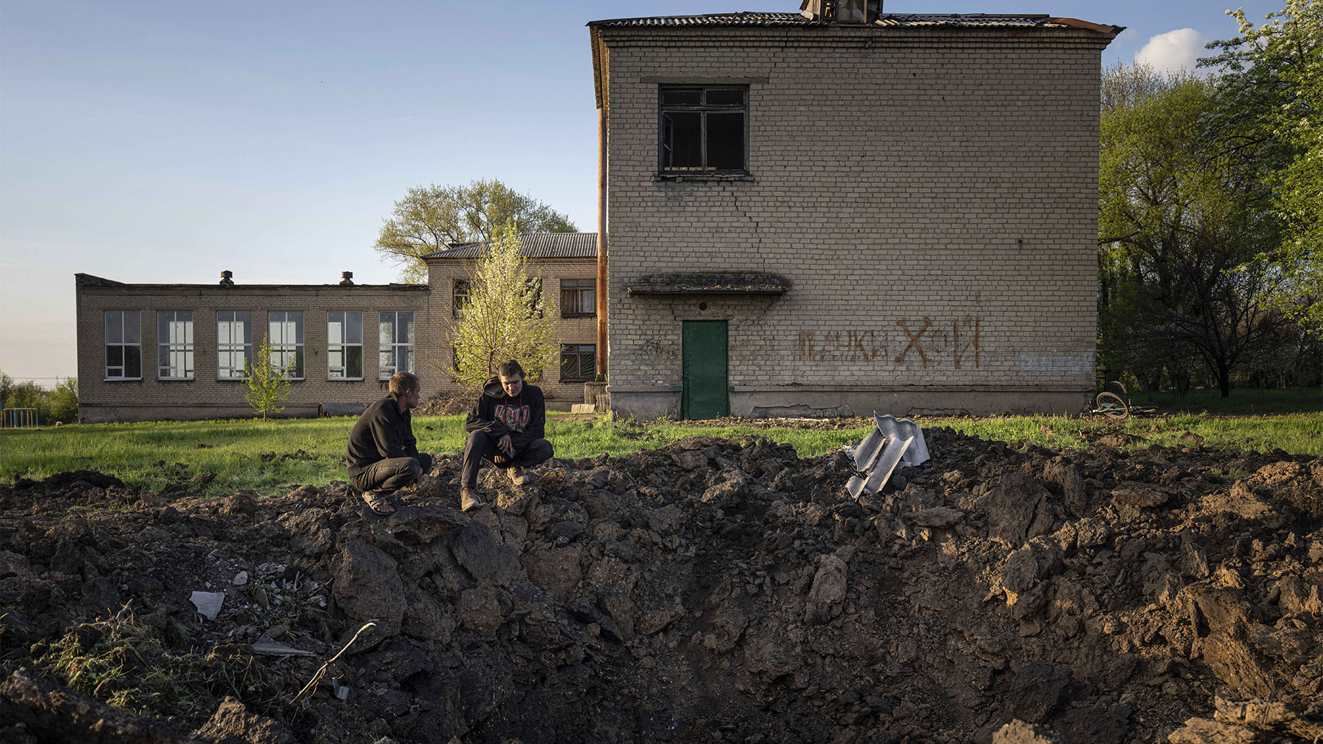 ARCHIVO - La gente mira un cráter creado por un ataque con cohetes rusos en el patio de una escuela en Dobropillya, región de Donetsk, este de Ucrania, el jueves 28 de abril de 2022. A pesar del daño generalizado y la destrucción de la infraestructura educativa, los expertos en crímenes de guerra dicen que demuestra la intención para las escuelas individuales es difícil. (Foto AP/Evgeniy Maloletka, archivo)