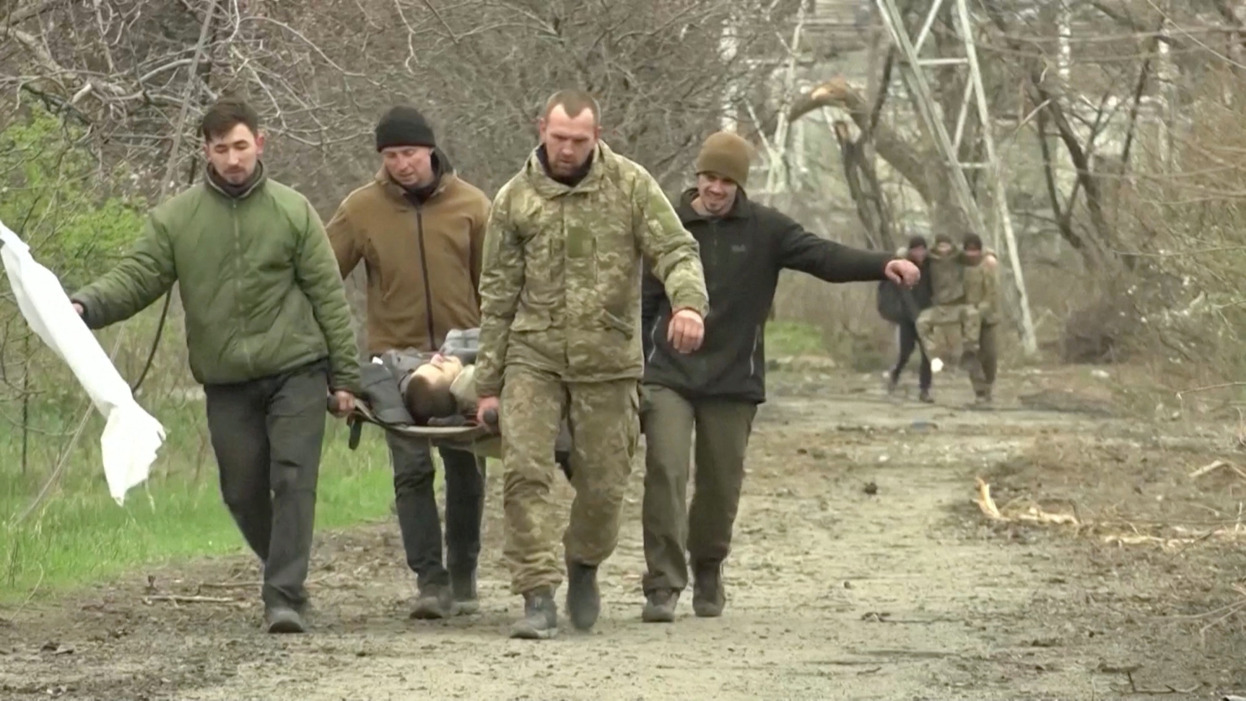 Los soldados llevan a un hombre herido en una camilla mientras muestran una bandera blanca en un lugar designado como Mariupol