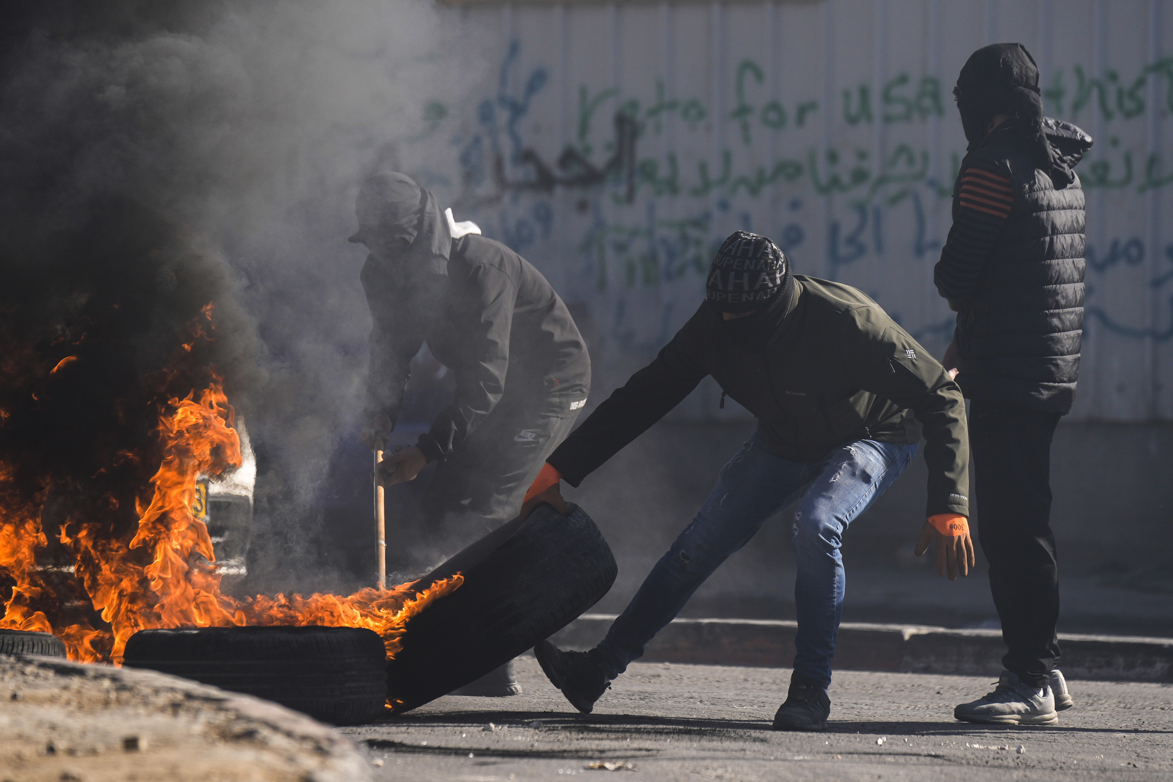 Manifestantes con el rostro cubierto incendian neumáticos durante una protesta contra una letal redada de soldados israelíes tras el funeral de Yusef Muhaisen en la ciudad cisjordana de al-Ram, al norte de Jerusalén, el viernes 27 de enero de 2023. (AP Foto/Majdi Mohammed)