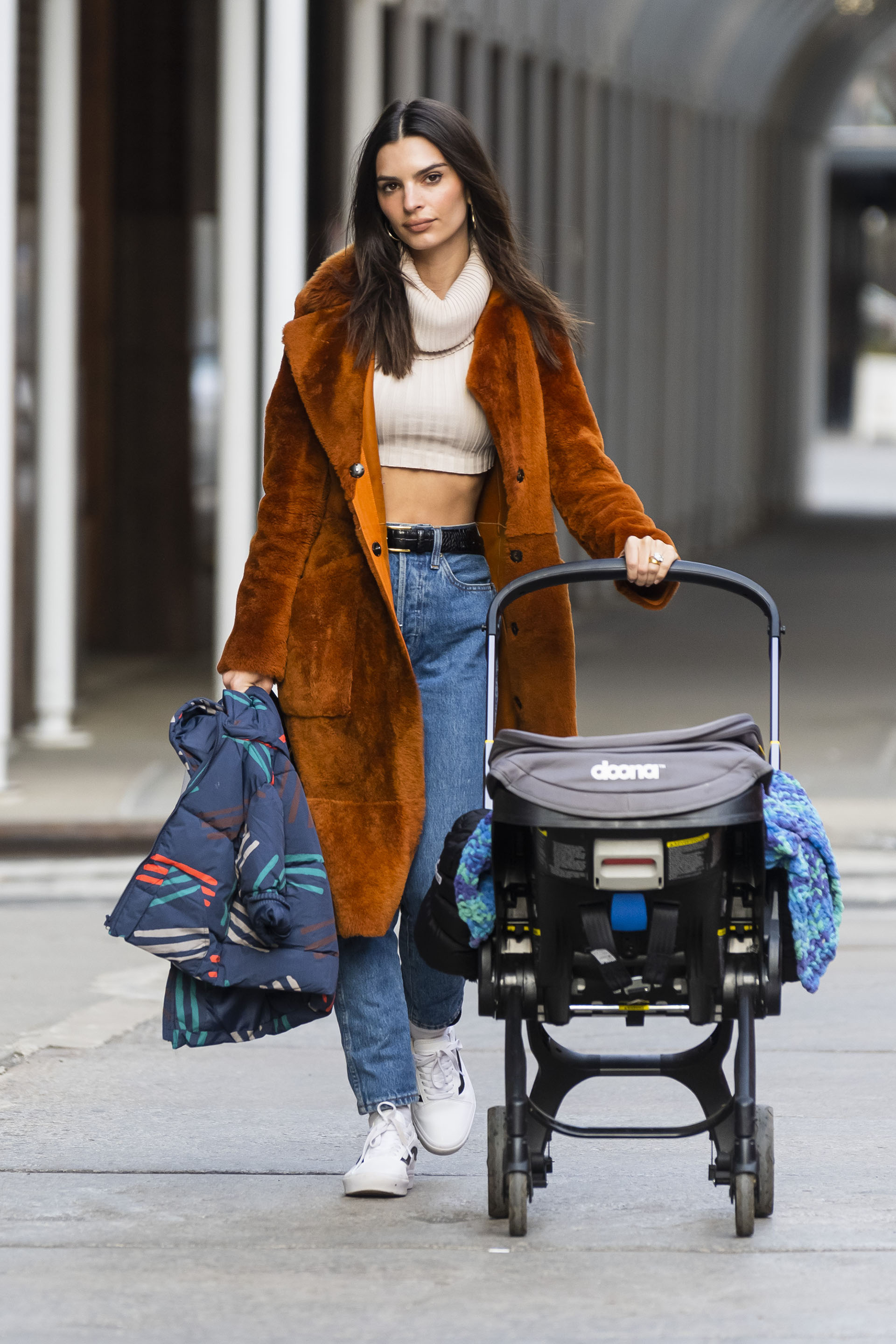 Emily Ratajkowski fue fotografiada durante un paseo por las calles de Nueva York con su bebé, quien fue en el cochecito. Lució un jean, una polera corta blanca de lana y un tapado marrón de piel sintética