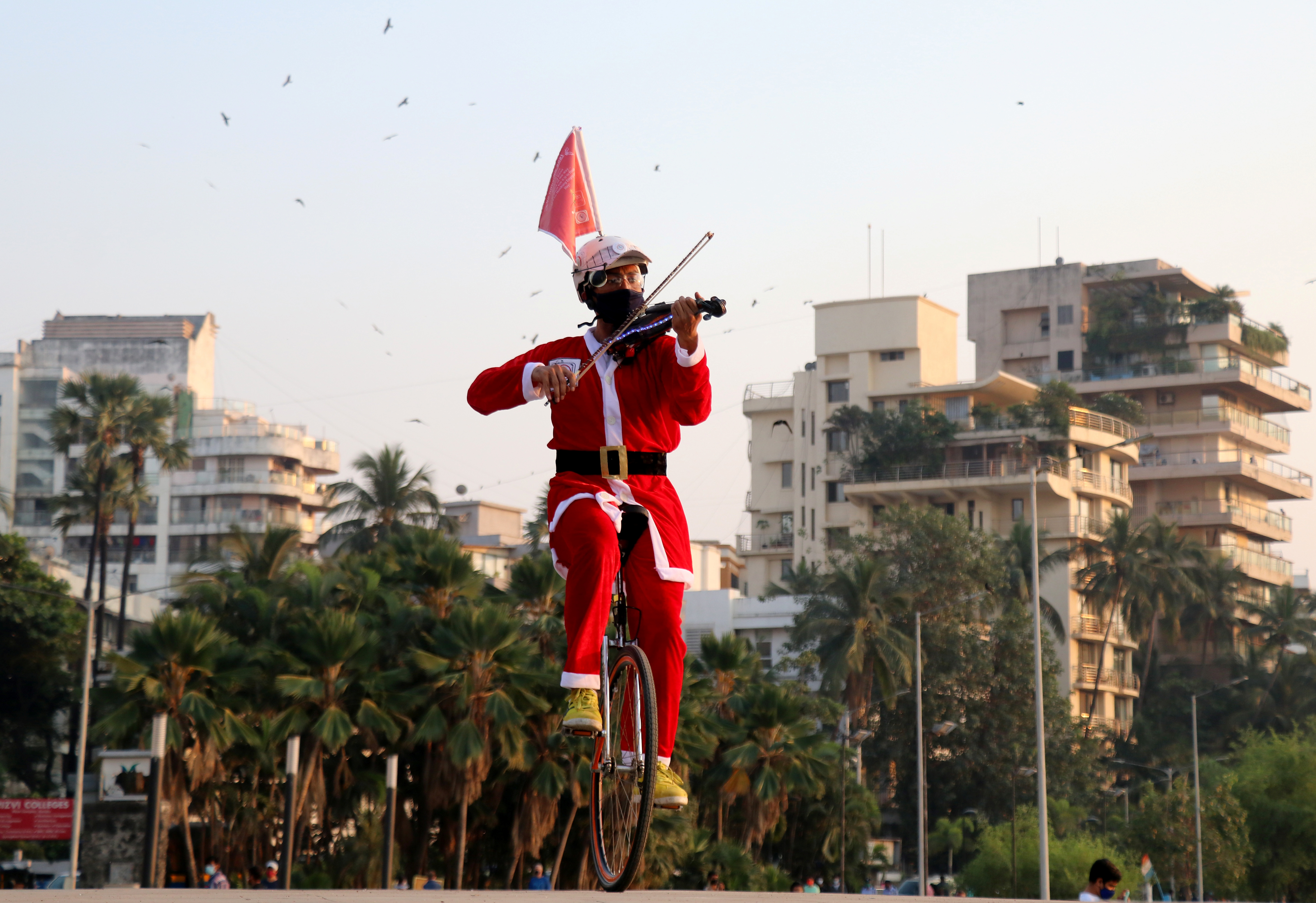 Un artista con un disfraz de Papá Noel monta un monociclo mientras toca un violín a lo largo de un paseo en Mumbai, India (REUTERS/Niharika Kulkarni)