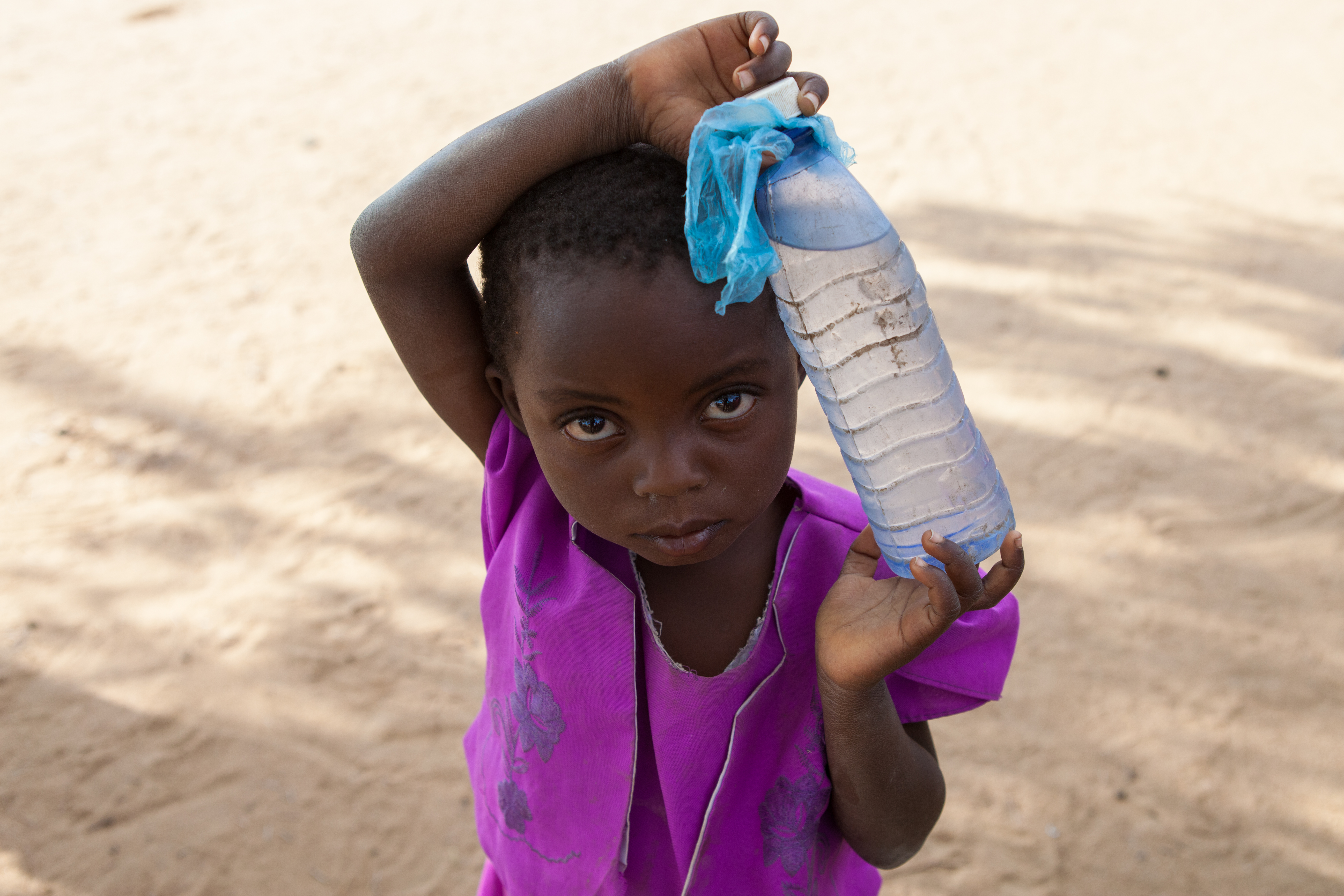 Una niña de 5 años, con un vestido morado, lleva una botella de agua de plástico en un pequeño pueblo del distrito sur de Nsanje, Malawi.
