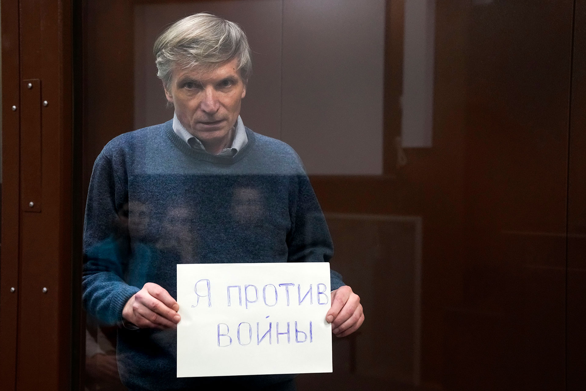 Alexei Gorinov sostiene un cartel "Estoy en contra de la guerra" de pie en una jaula durante la audiencia en la sala del tribunal en Moscú, Rusia, el 21 de junio de 2022 (AP/Archivo)