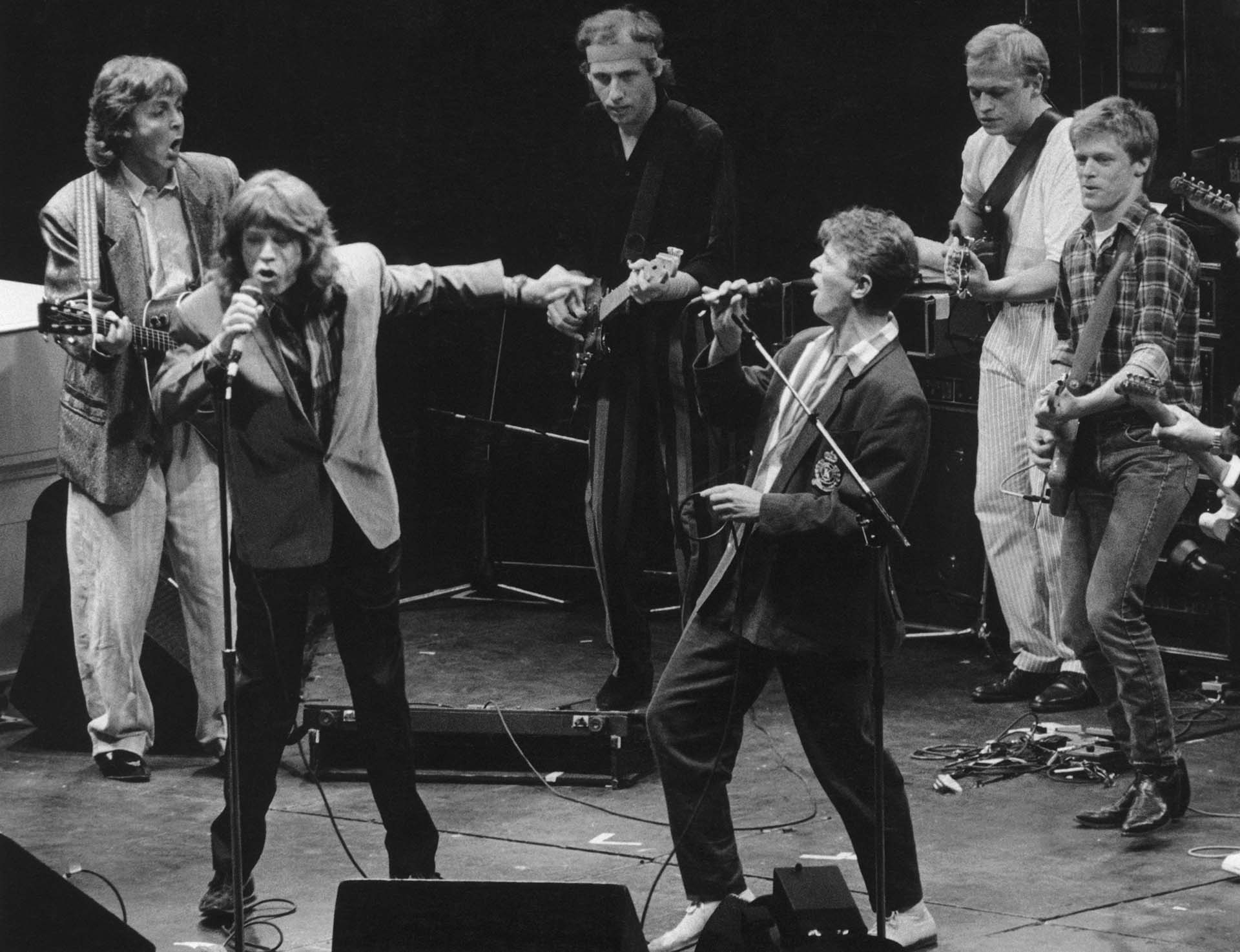 Mick Jagger y David Bowie cantan junto a una banda de estrellas entre las que aparece Paul McCartney, el primero de izquierda, junto a Mark Knopfler, Mark King y Brian Adams en Wembley, el 23 de junio de 1986 (Photo by Dave Hogan/Hulton Archive/Getty Images)
