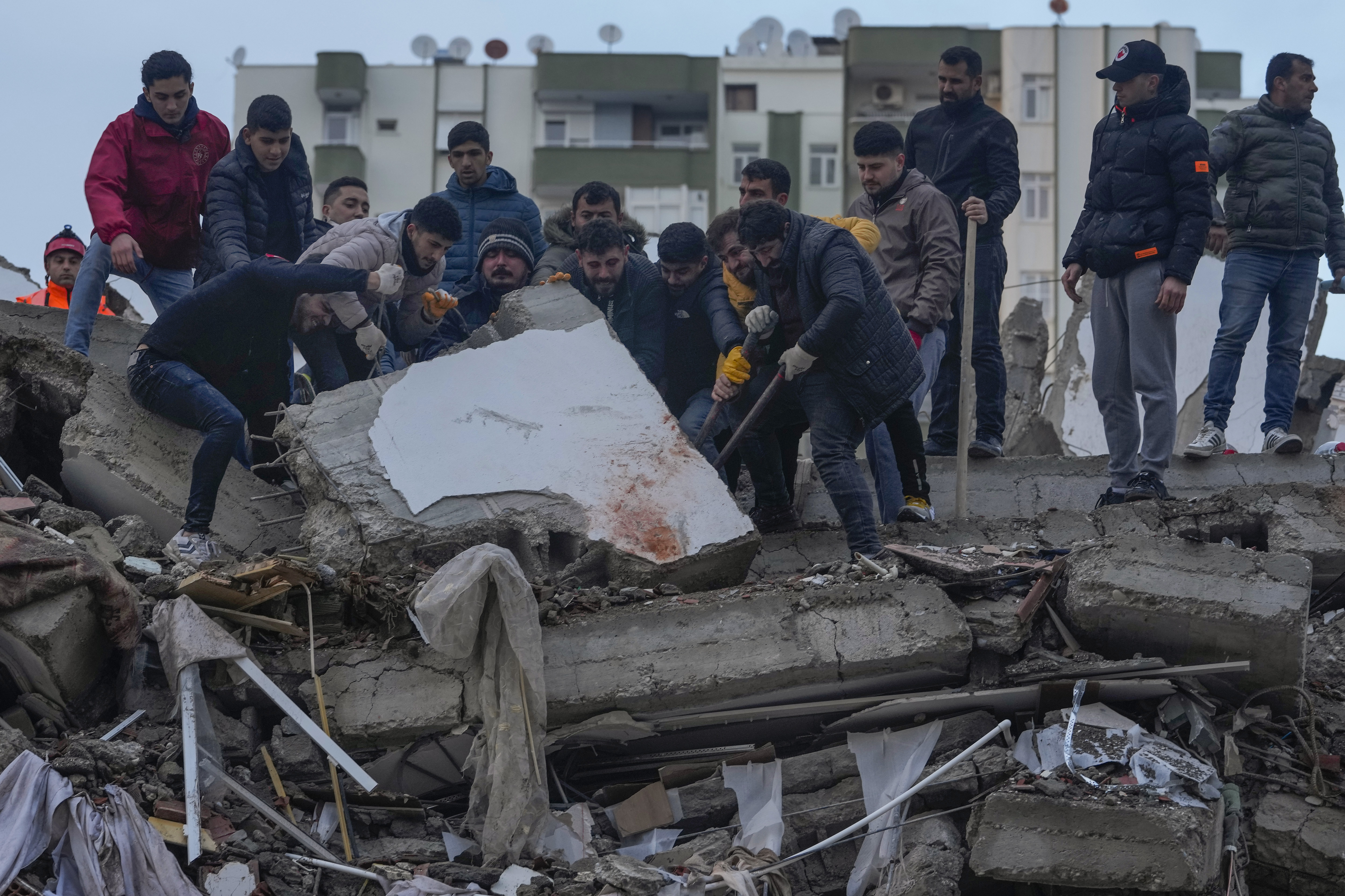 Un grupo de personas busca entre los escombros de un edificio a sobrevivientes tras un sismo, en Adana, Turquía, el lunes 6 de febrero de 2023. (AP Foto/Khalil Hamra)