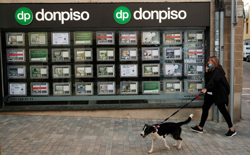 Una mujer con mascarilla camina con un perro frente a una oficina de la agencia inmobiliaria Don Piso.