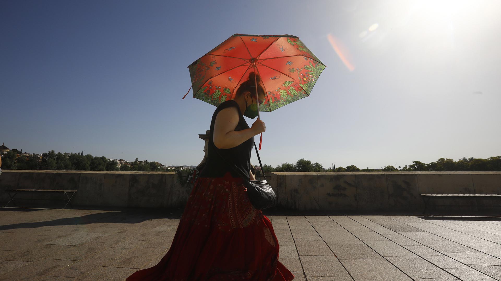 Una mujer se protege con un paraguas de las altas temperaturas mientras pasea por el puente Romano de Córdoba (EFE)

