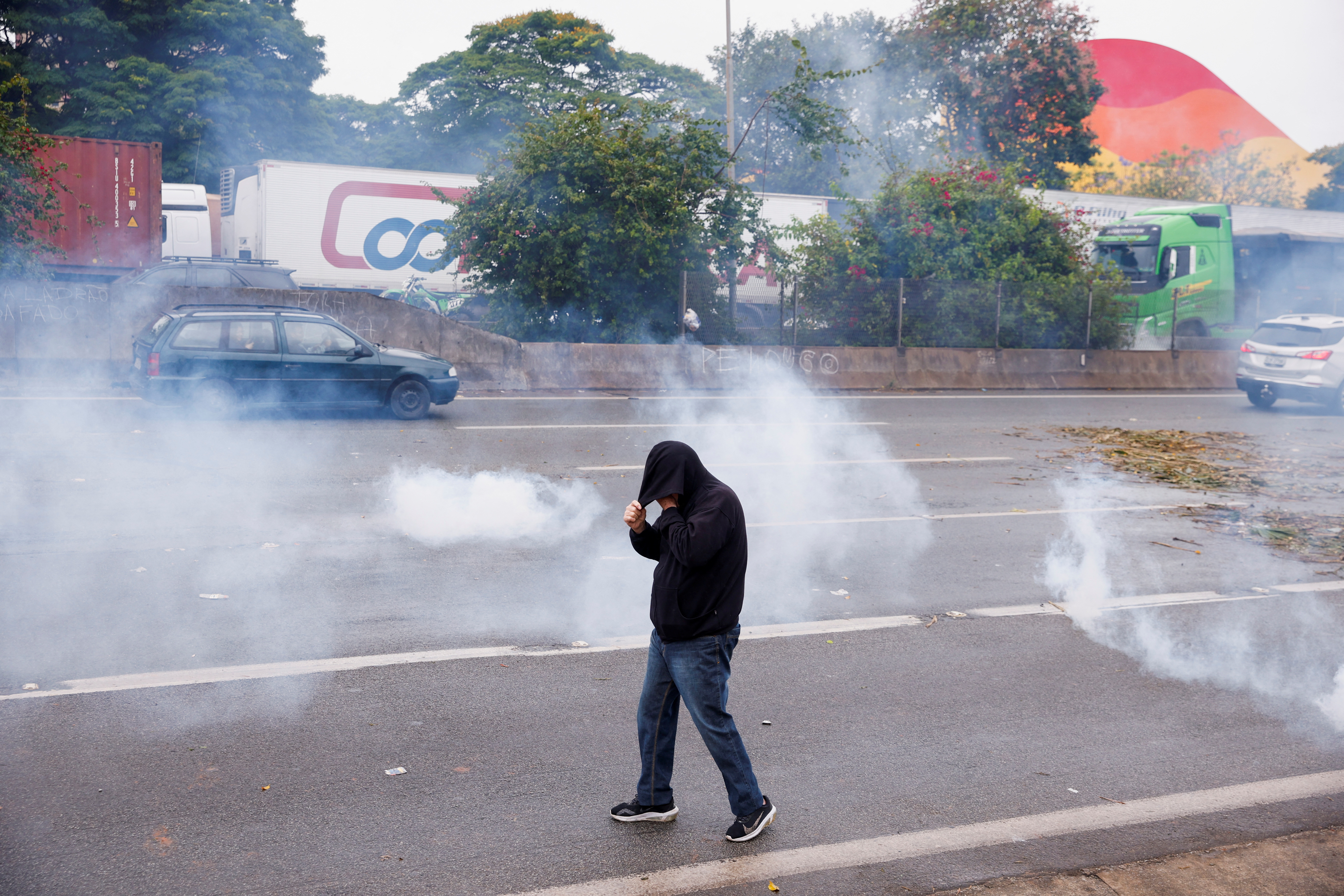 Un partidario del presidente de Brasil, Jair Bolsonaro, intenta cubrirse la cara mientras se encuentra en medio de botes de gas lacrimógeno durante una protesta 