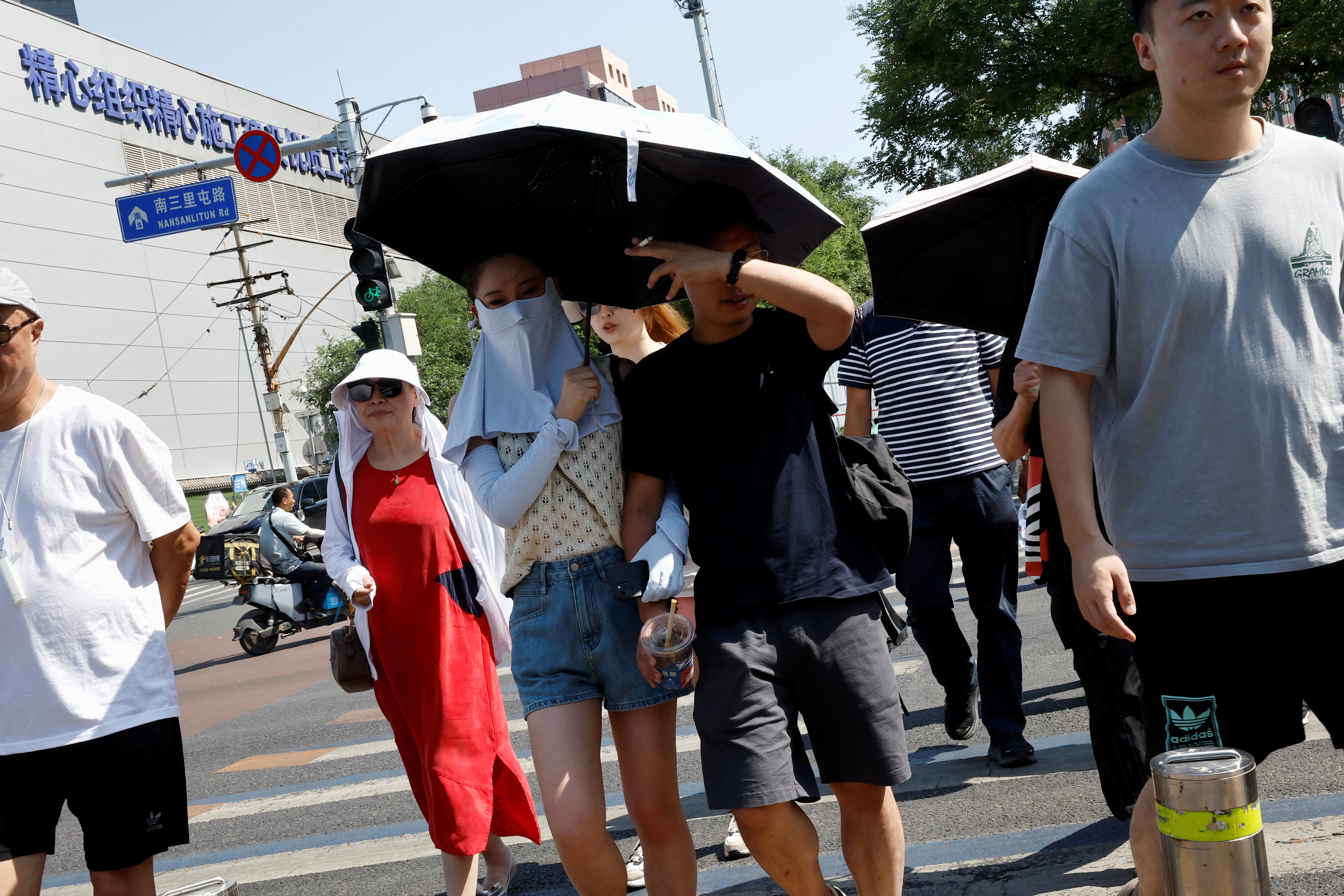 La gente se protege con sombrillas y máscaras faciales del sol en medio de una alerta naranja por ola de calor en Beijing, China, el 22 de junio de 2023. REUTERS/Tingshu Wang